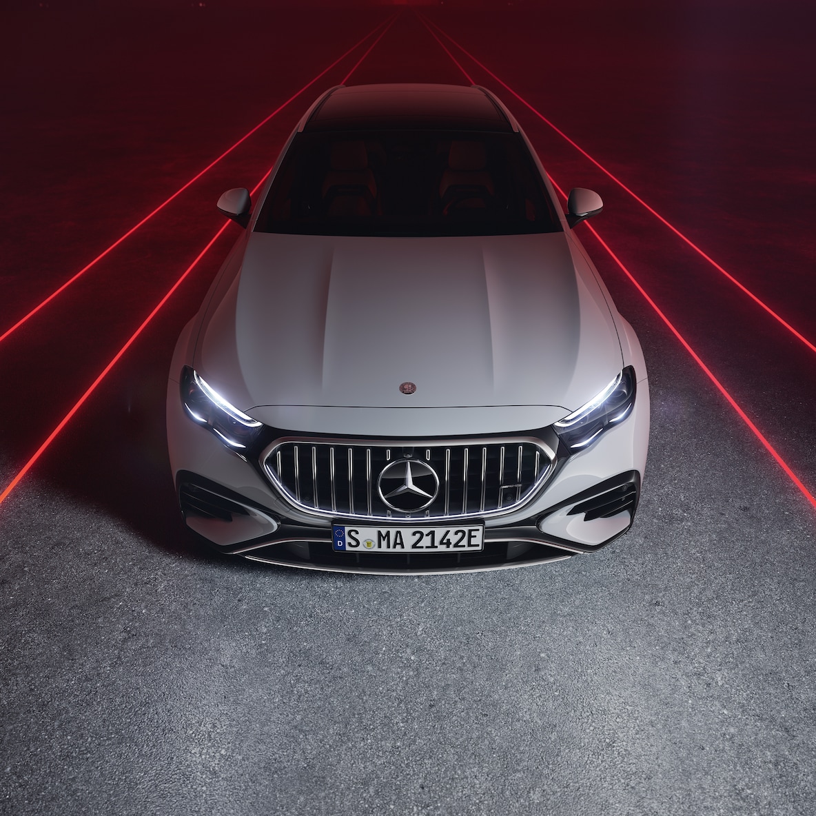 A Mercedes-AMG E 53 HYBRID 4MATIC+ elölnézetben, piros háttér előtt, felülről nézve.
