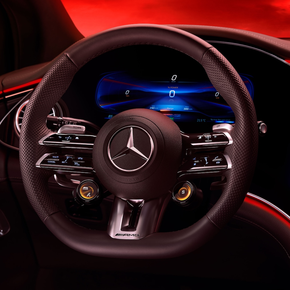 Az AMG Performance kormánykerék képe a vezetőülésből nézve, piros háttér előtt.