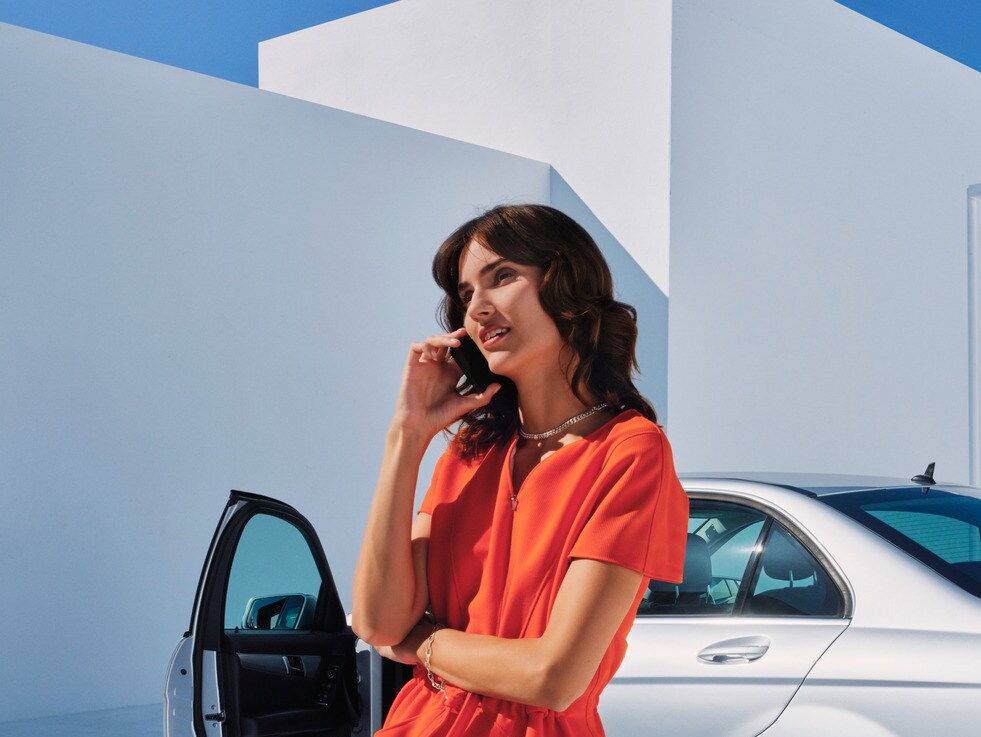 Egy nő telefonál a Mercedes-Benz gépkocsija előtt