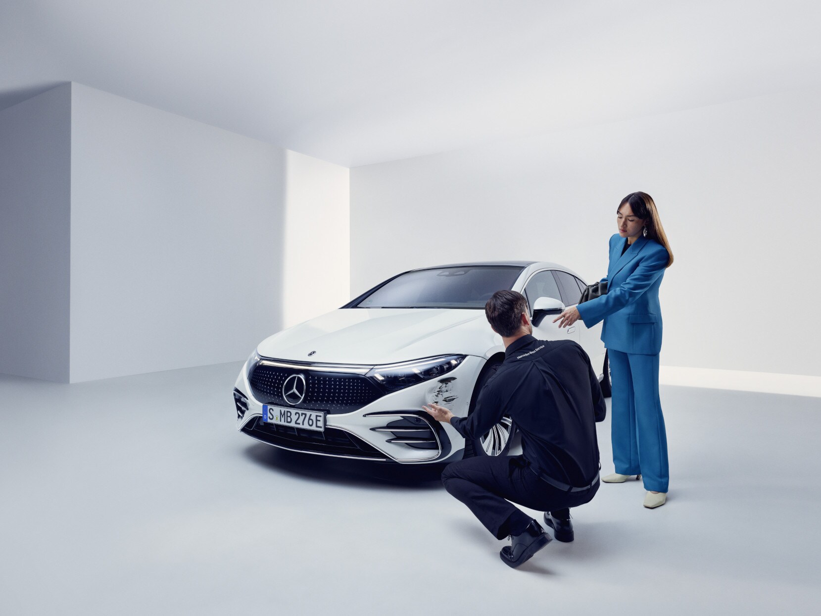 A Mercedes-Benz ügyfélszolgálatának munkatársa térdel egy sérült Mercedes-Benz mellett.