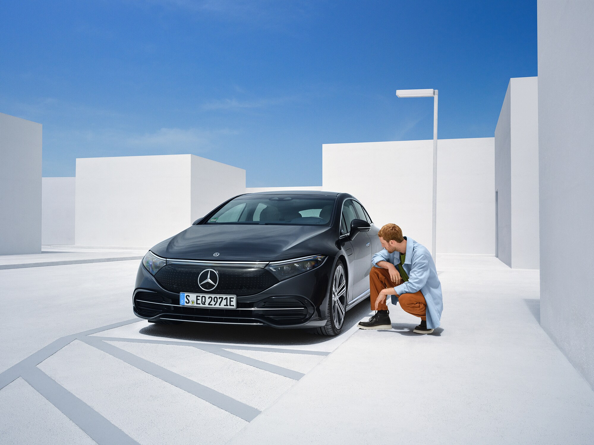 Egy férfi Mercedes-Benz modellje mellett térdel, hogy ellenőrizze azt