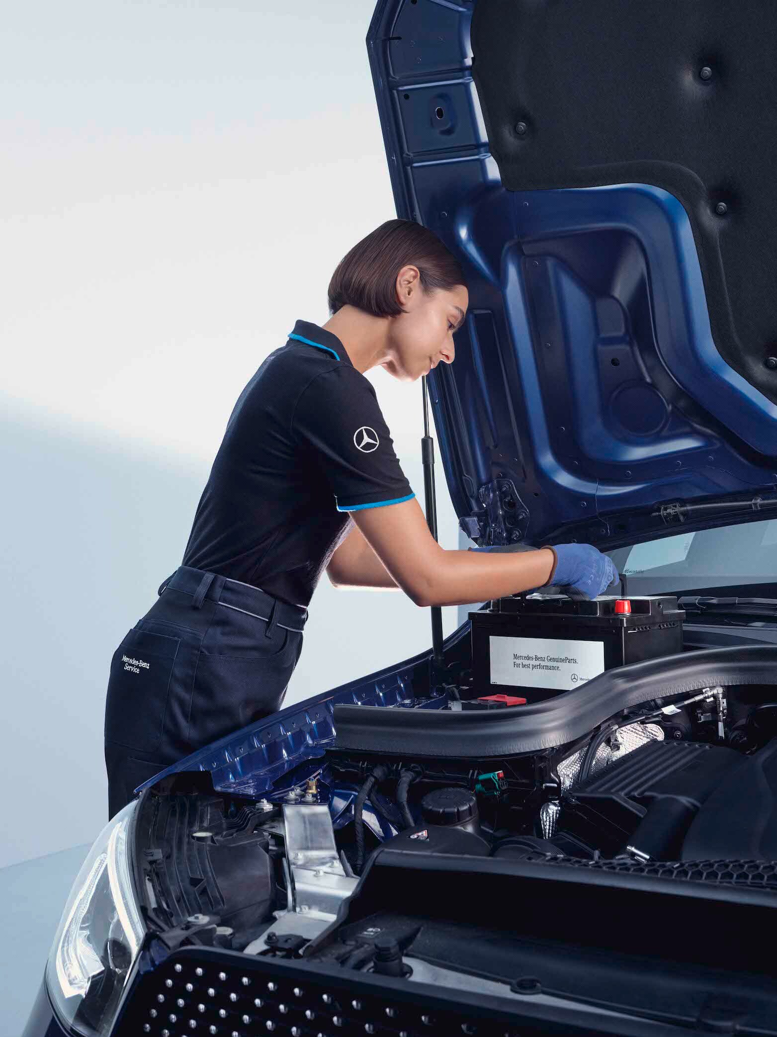 Egy szerelő egy Mercedes-Benz modell nyitott motorháztetője fölé hajol.