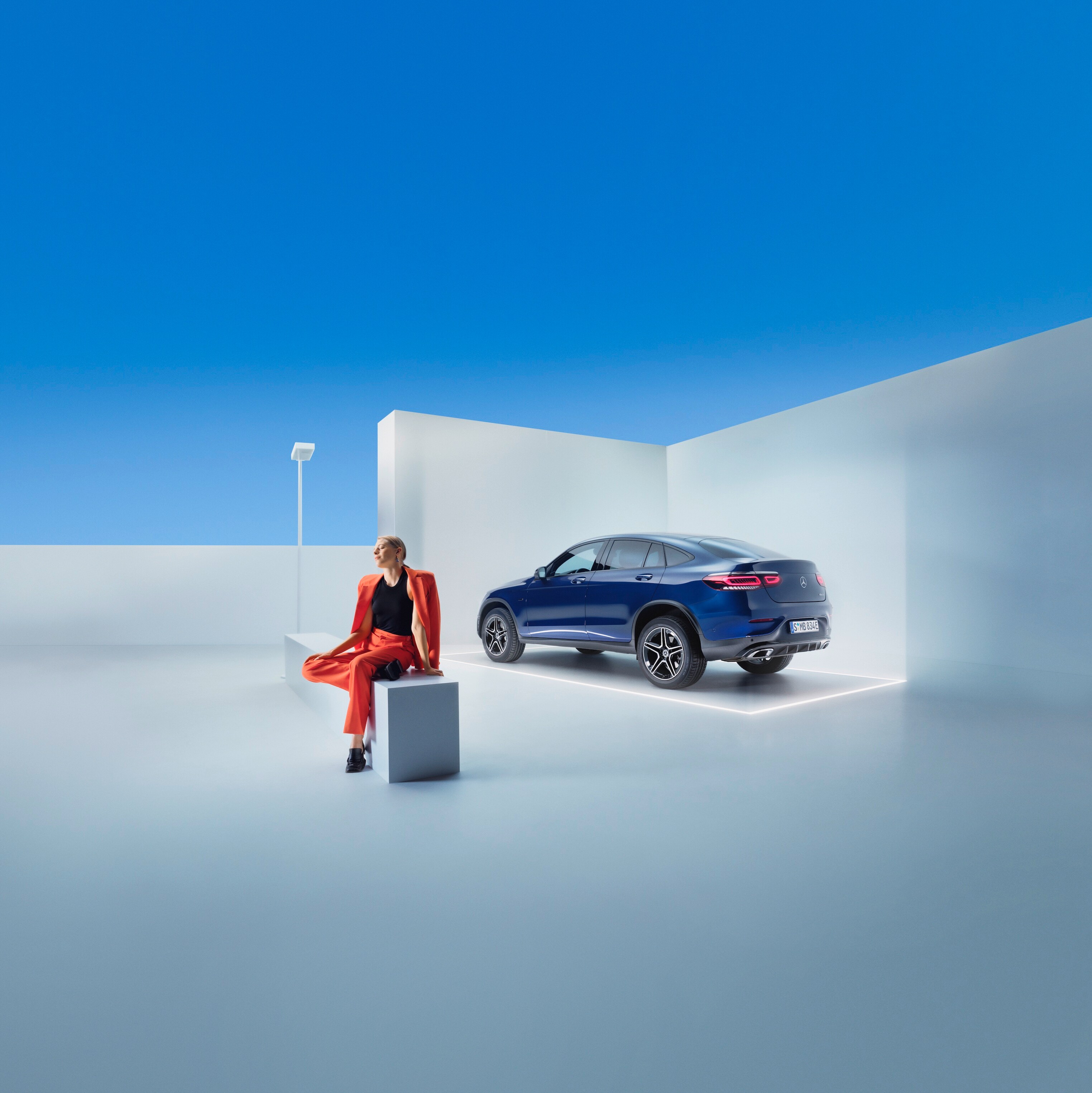 Egy nő ül egy padon egy Mercedes-Benz előtt.