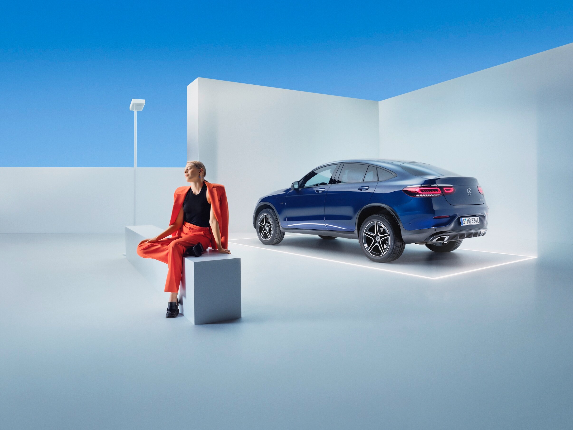 Egy nő ül egy padon egy Mercedes-Benz előtt.