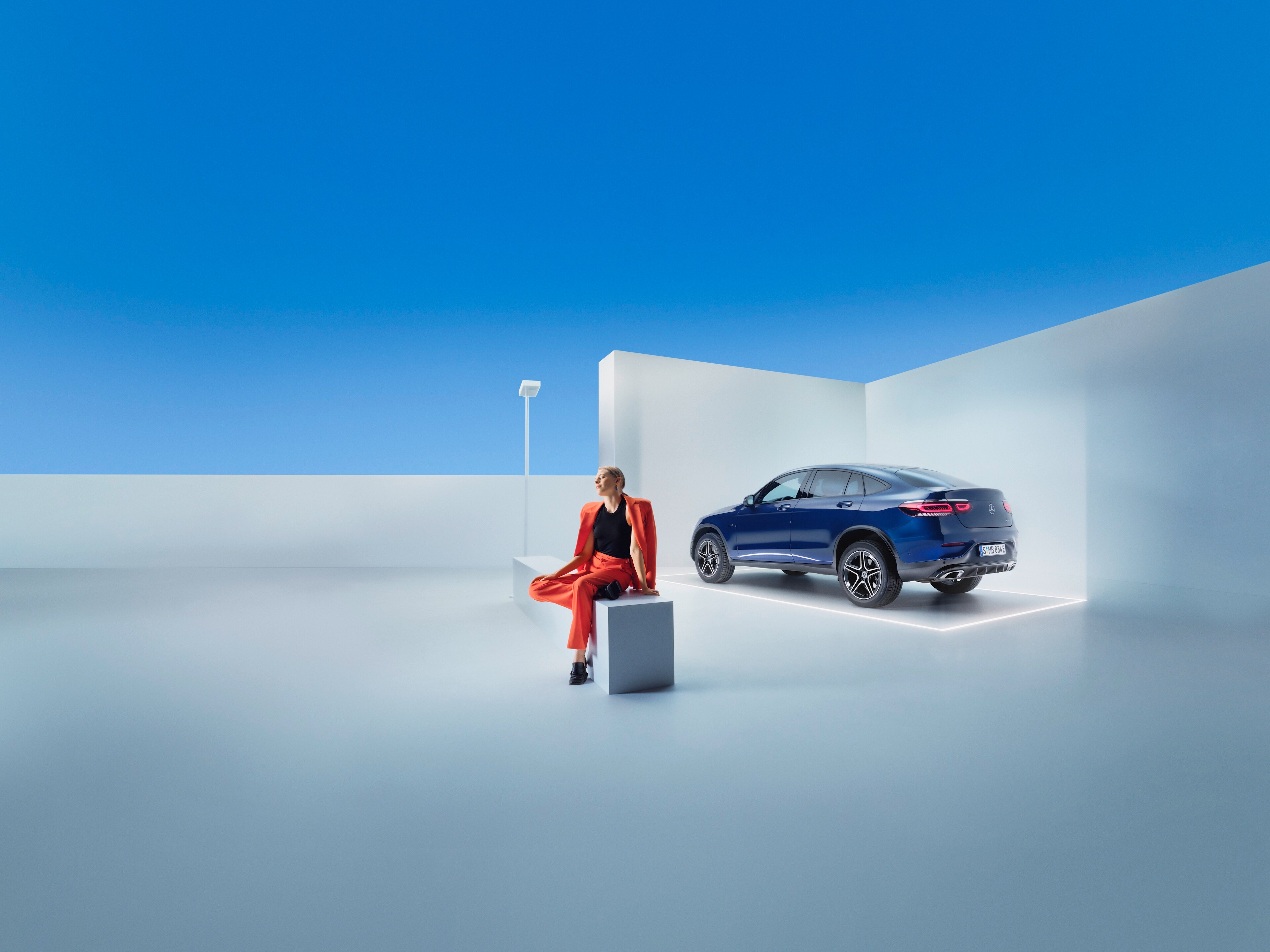 Egy nő ül egy padon egy Mercedes-Benz előtt.