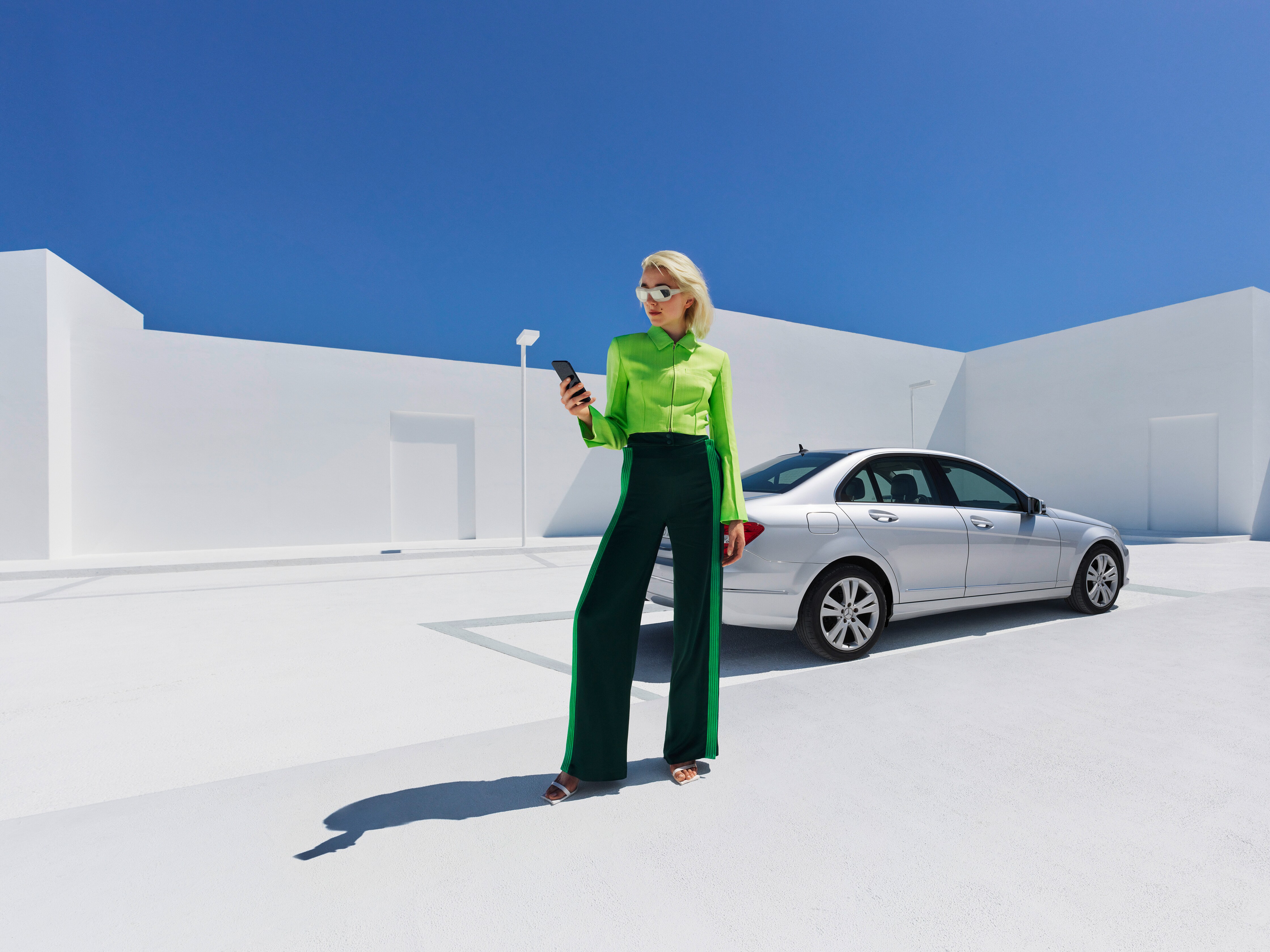 Egy nő a telefonját nézi, miközben a Mercedes-Benz autója előtt áll.