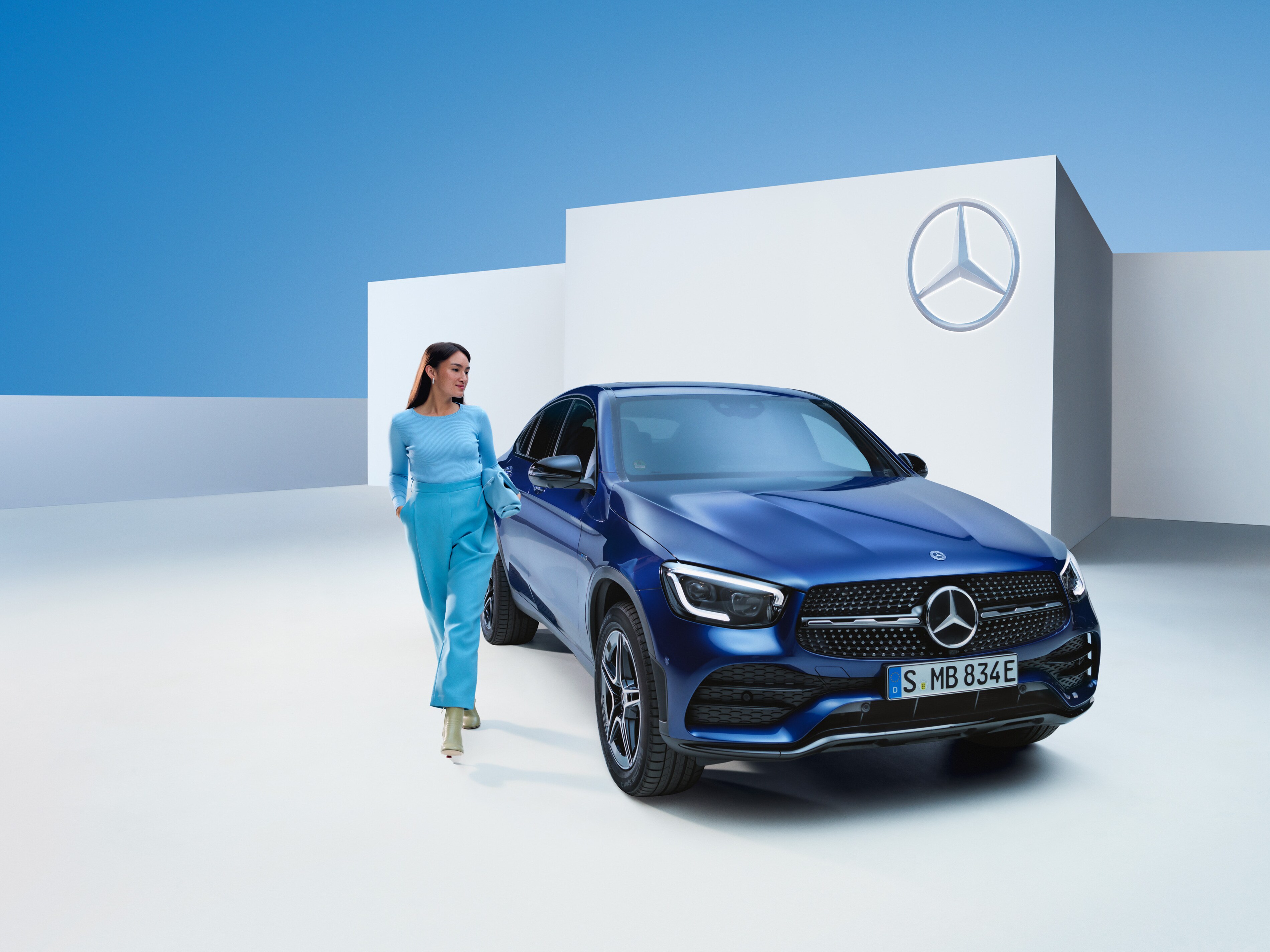 Egy nő sétál a Mercedes-Benz autója mellett.