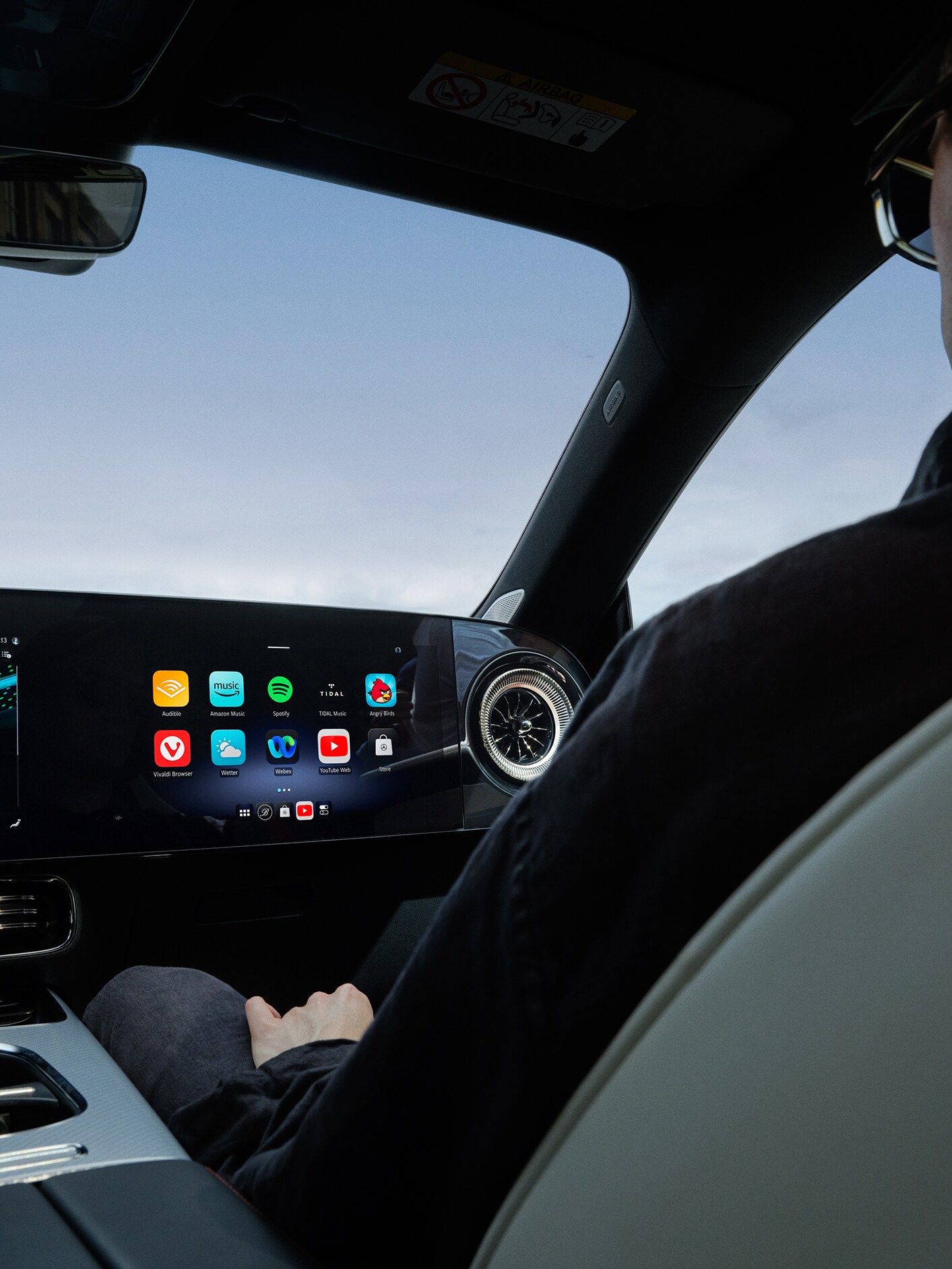 Belső nézet egy Mercedes-Benz személygépkocsi MBUX multimédia-rendszerrel felszerelt vezetőfülkéjéről.