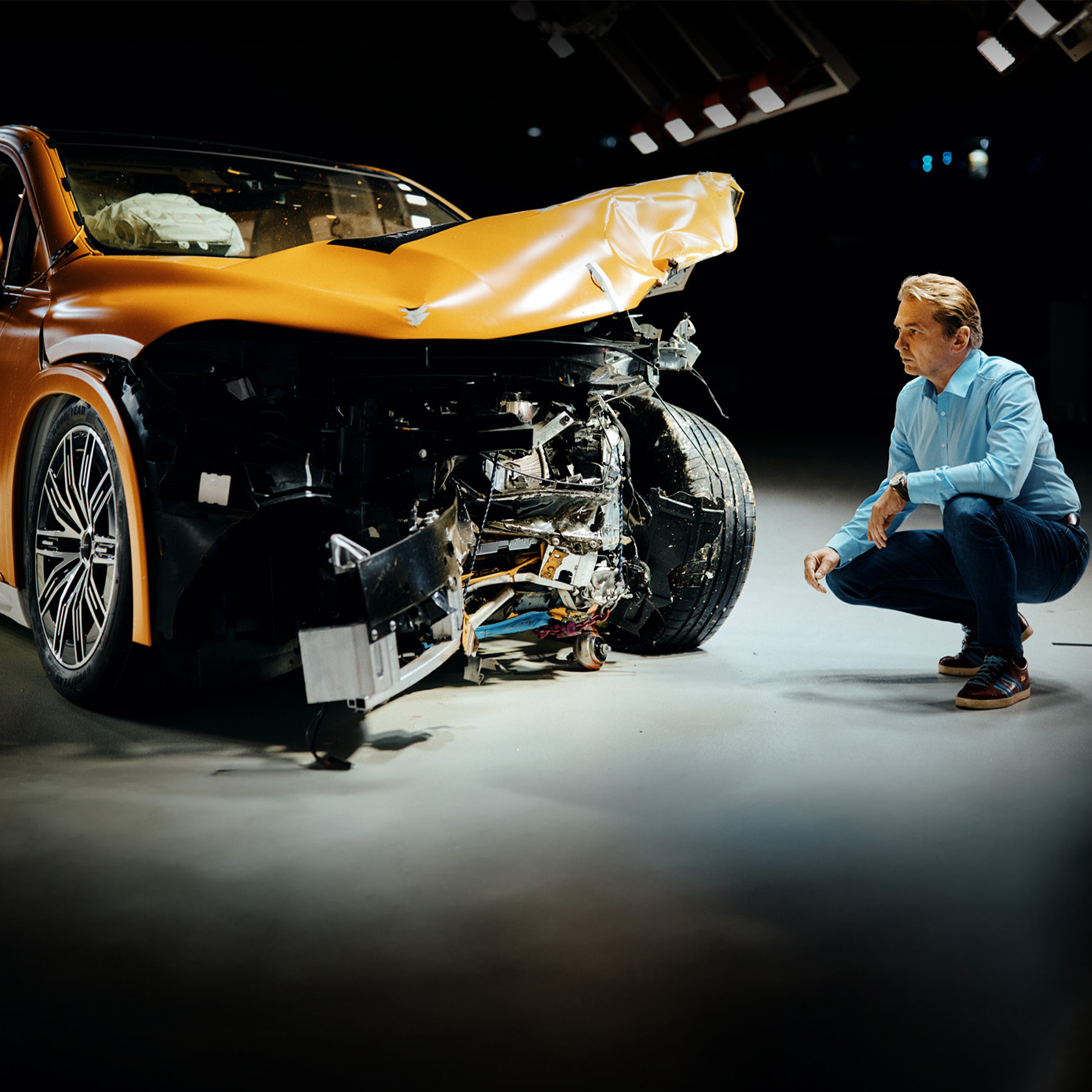 Törésteszt-szakértők | Biztonság | Mercedes-Benz Törésteszt-szakértő vizsgálja az elöl összetört Mercedes-Benz modellt, miközben mellette guggol.