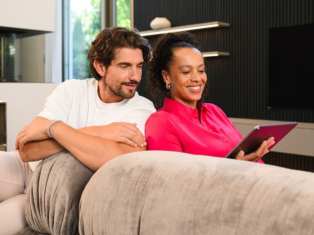 Két ember egy kanapén ülve egy mobilkészüléket néz.