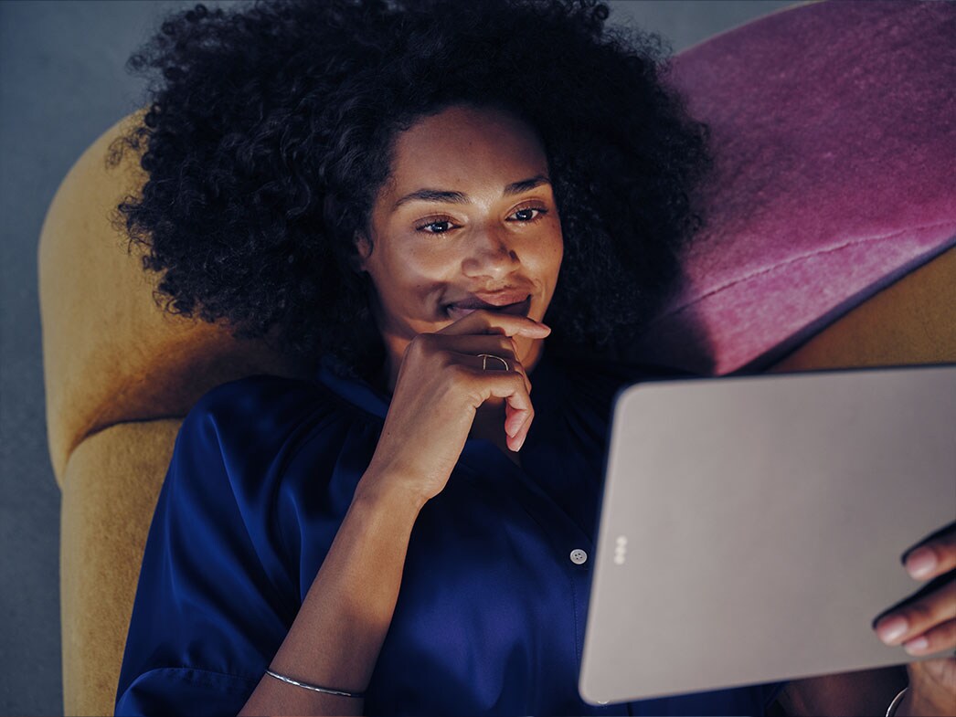 Egy nő ül egy kanapén és nézi a tabletjét