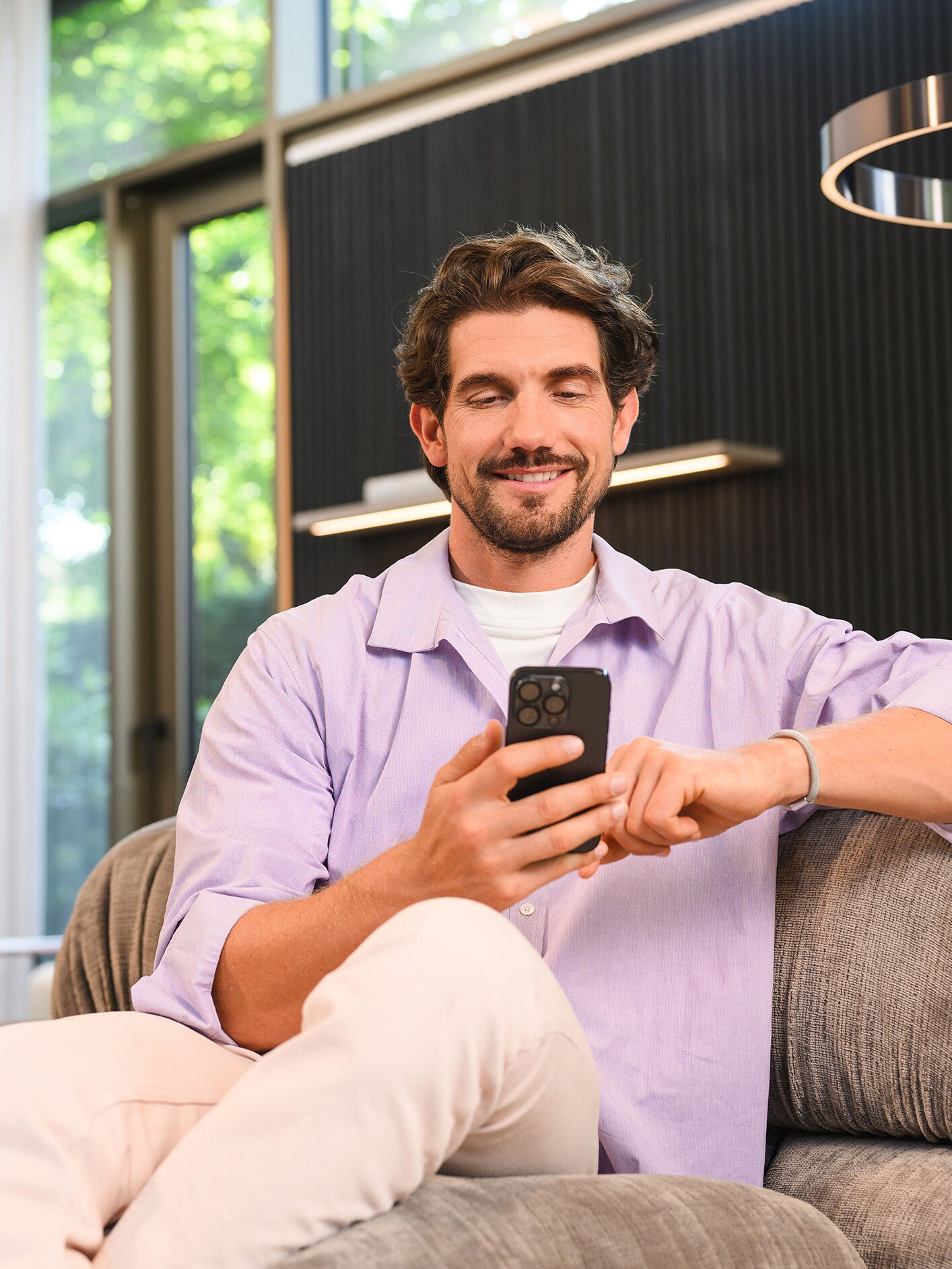 Egy ember a kanapén ülve a mobilkészülékét nézi.