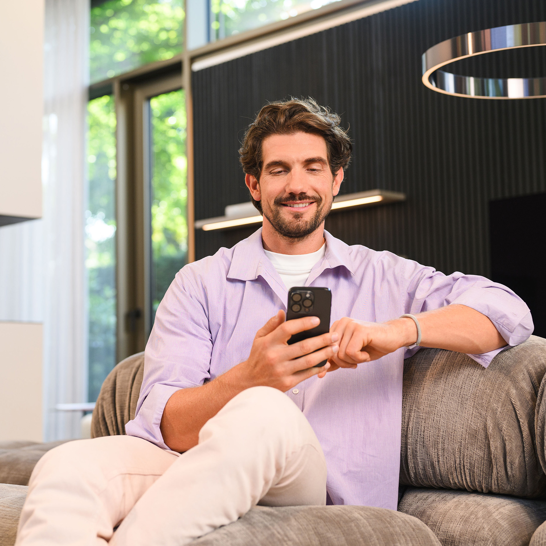 Biztosítás az Ön Mercedes-Benz Egy ember a kanapén ülve a mobilkészülékét nézi.