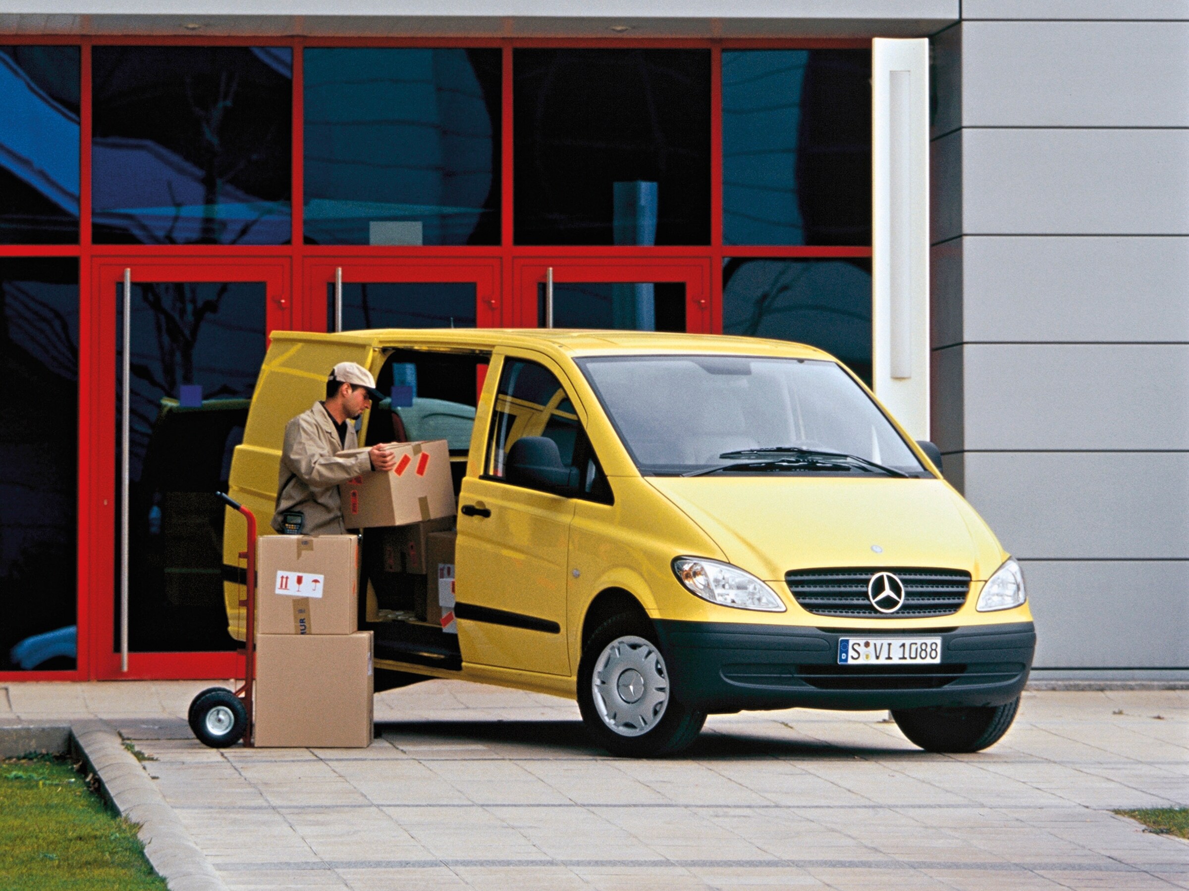 Egy épület előtt parkoló sárga Mercedes-Benz Vito, amelyből egy munkás csomagokat rakod ki