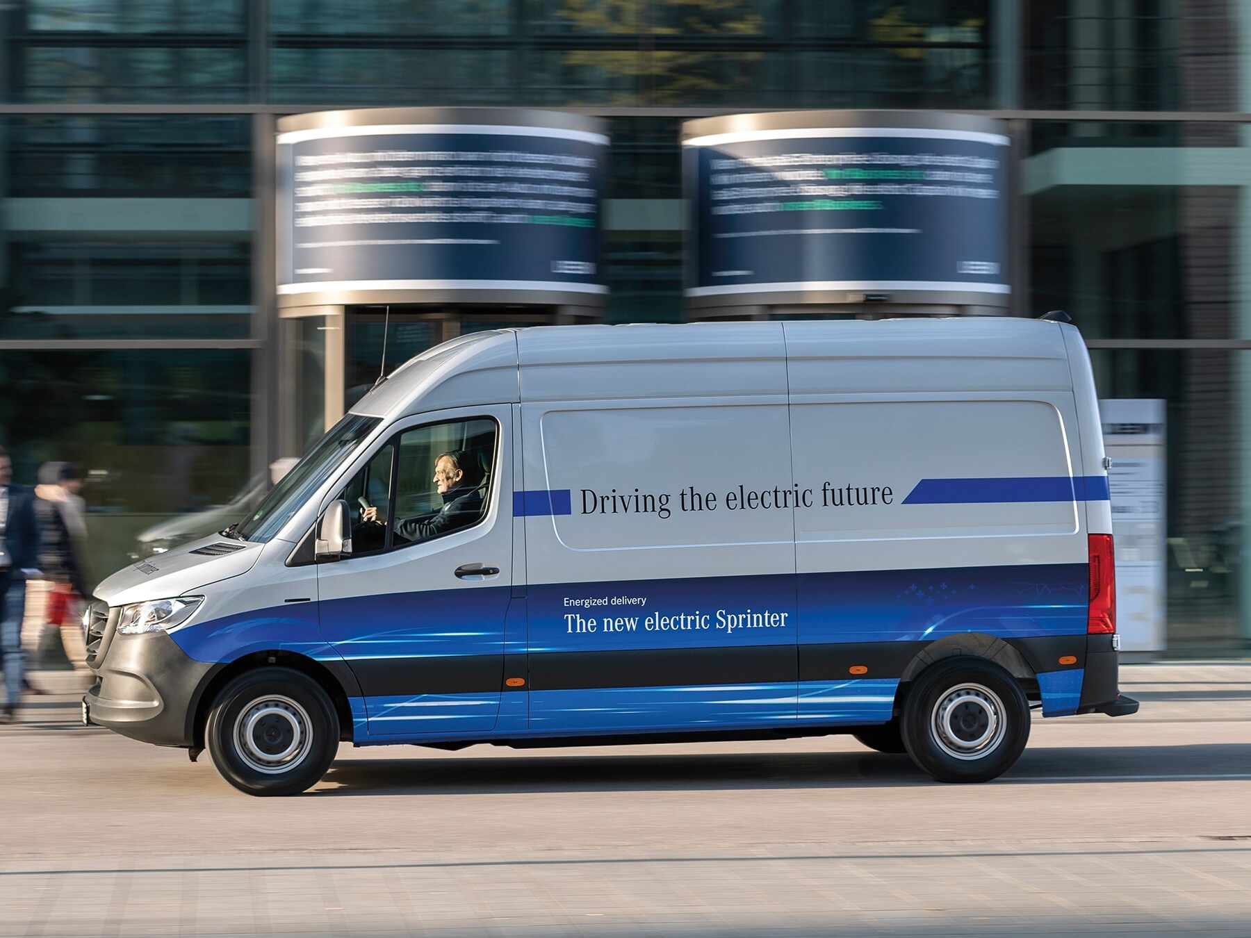 Egy Mercedes-Benz eSprinter zárt áruszállító halad egy modern városi utcán