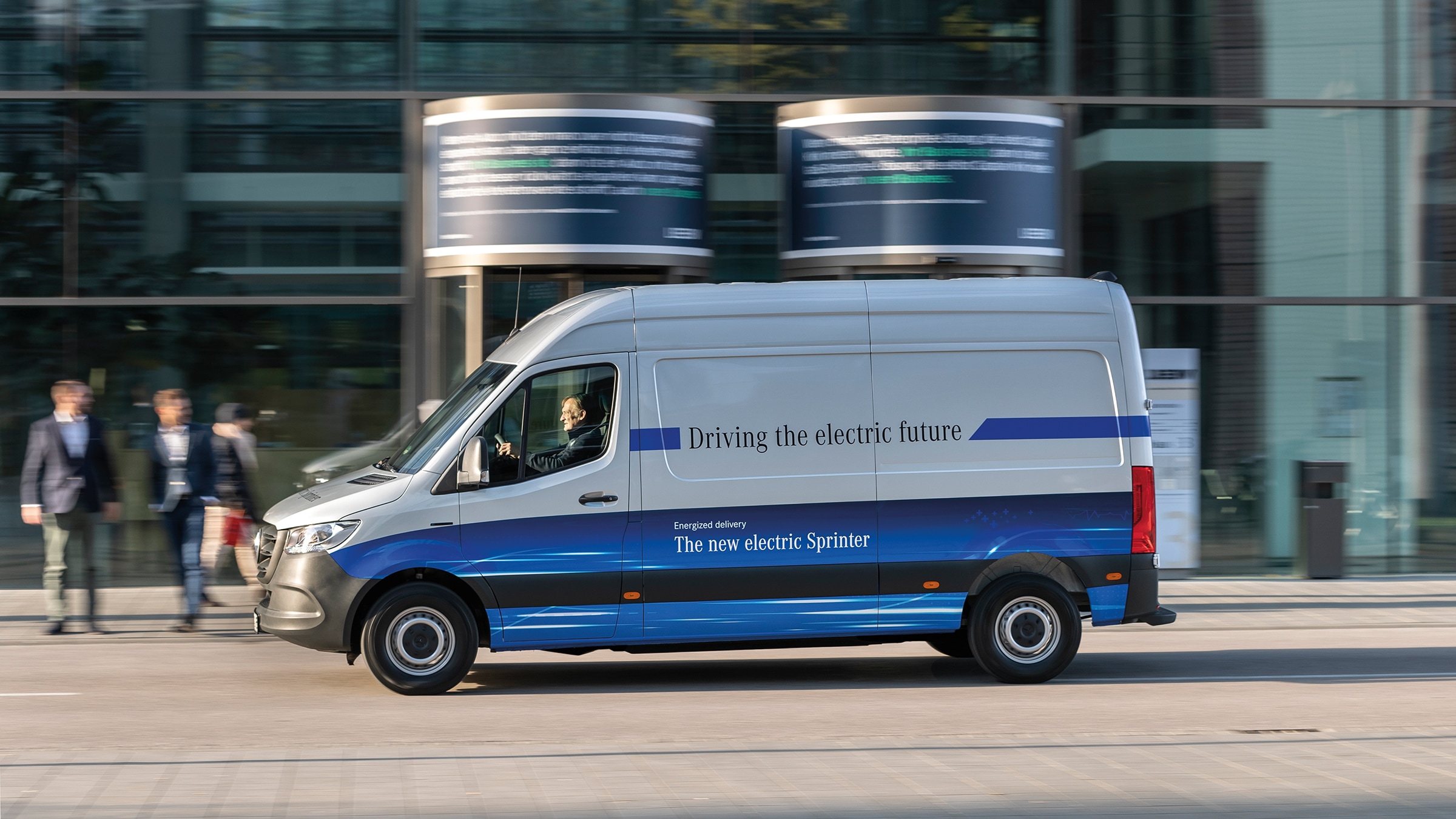 A második generációs eSprinter zárt áruszállító | Haszongépjárművek történelme | Mercedes-Benz Egy Mercedes-Benz eSprinter zárt áruszállító halad egy modern városi utcán