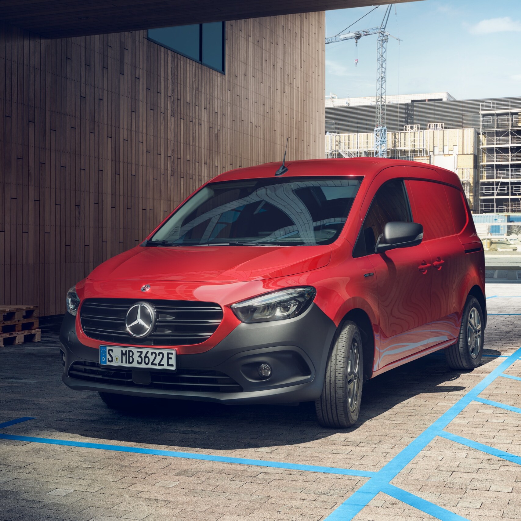 Az eCitan zárt áruszállító, a Mercedes-Benz elektromos kishaszongépjárműve egy töltőállomáson parkol egy ipari épület előtt.