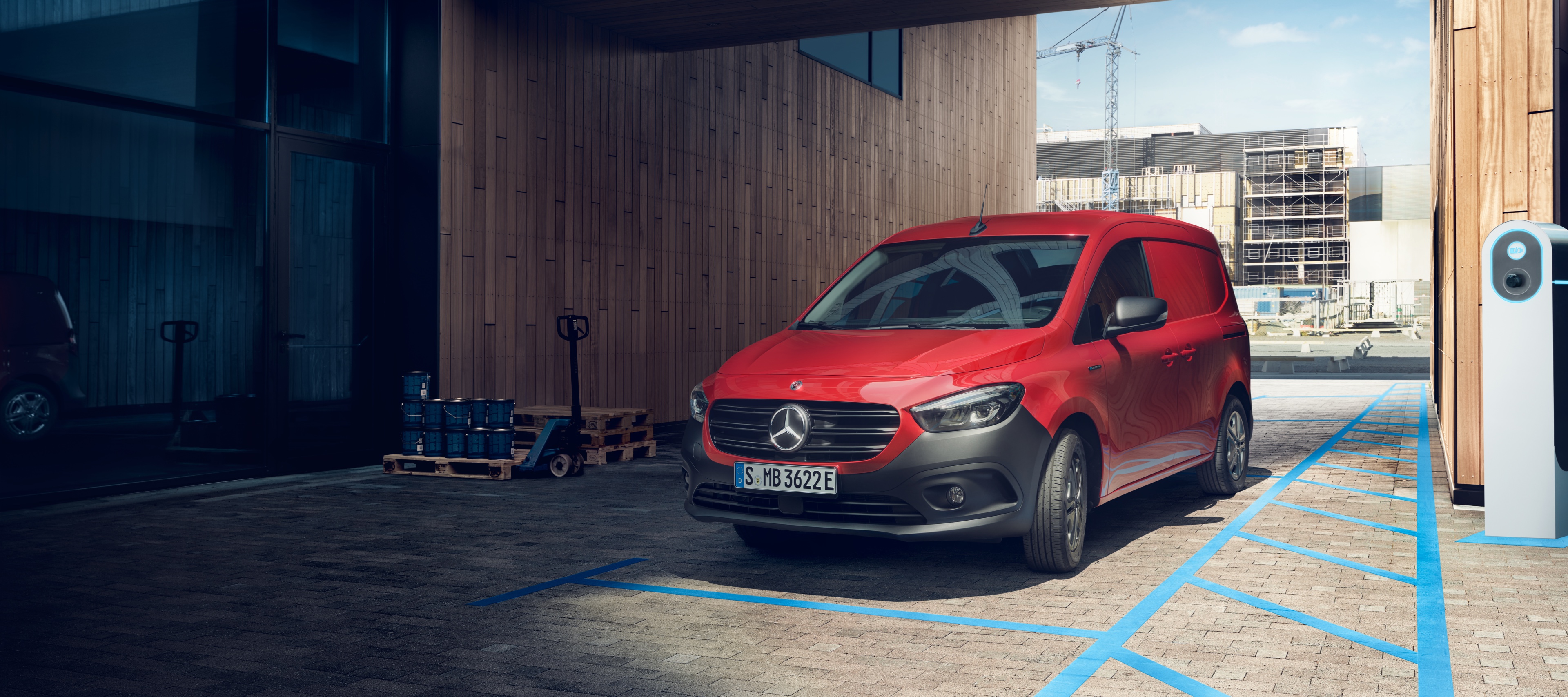 eCitan zárt áruszállító | Mercedes-Benz transzporter Az eCitan zárt áruszállító, a Mercedes-Benz elektromos kishaszongépjárműve egy töltőállomáson parkol egy ipari épület előtt.