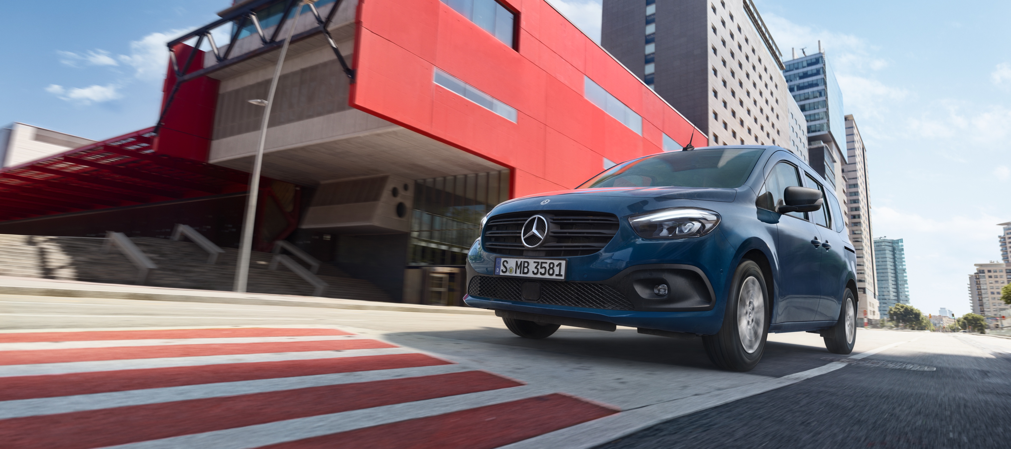 eCitan Tourer | Mercedes-Benz kishaszongépjárművek Az eCitan Tourer, a Mercedes-Benz elektromos személyszállító furgonja egy modern városi területen halad.