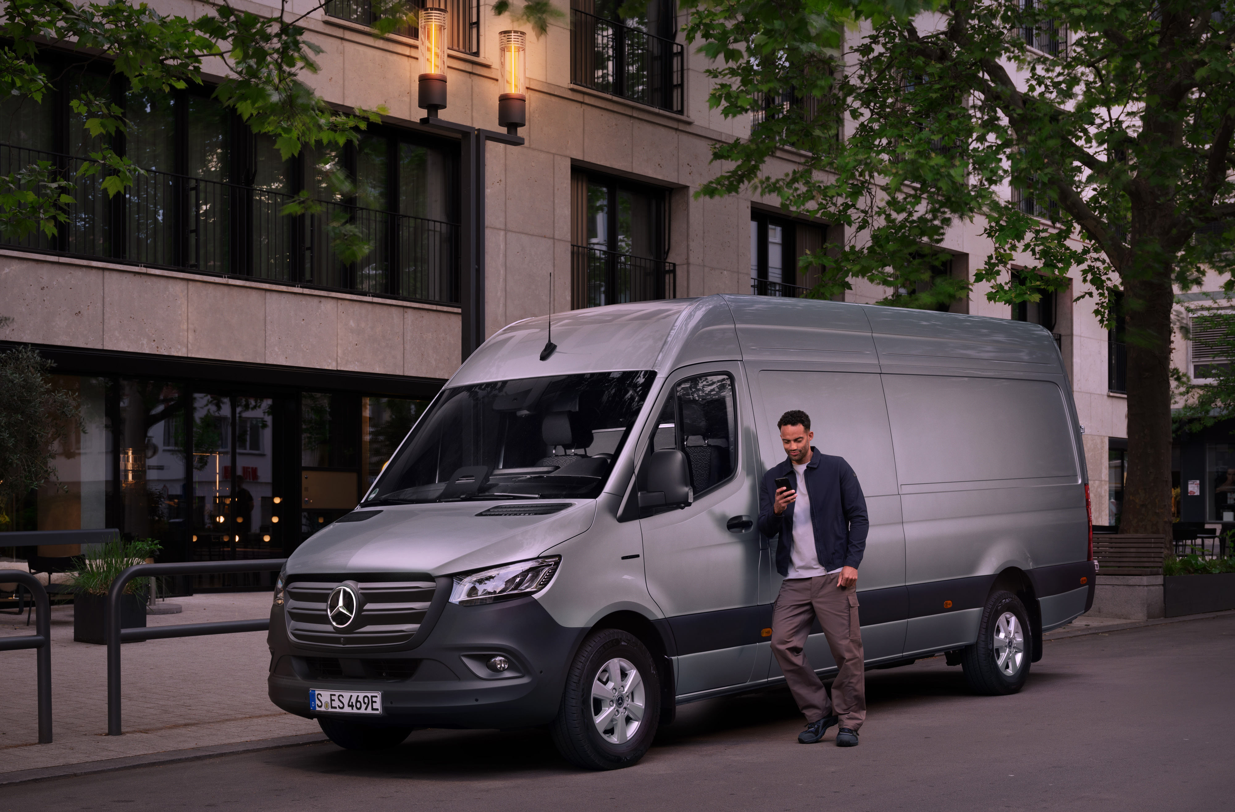Mercedes-Benz | Kishaszongépjármű szolgáltatás | Customer Assistance Center Egy ezüstszínű Mercedes-Benz Sprinterre támaszkodó férfi az okostelefonját használja - gyors segítség a Mercedes-Benz ügyfélszolgálattól.