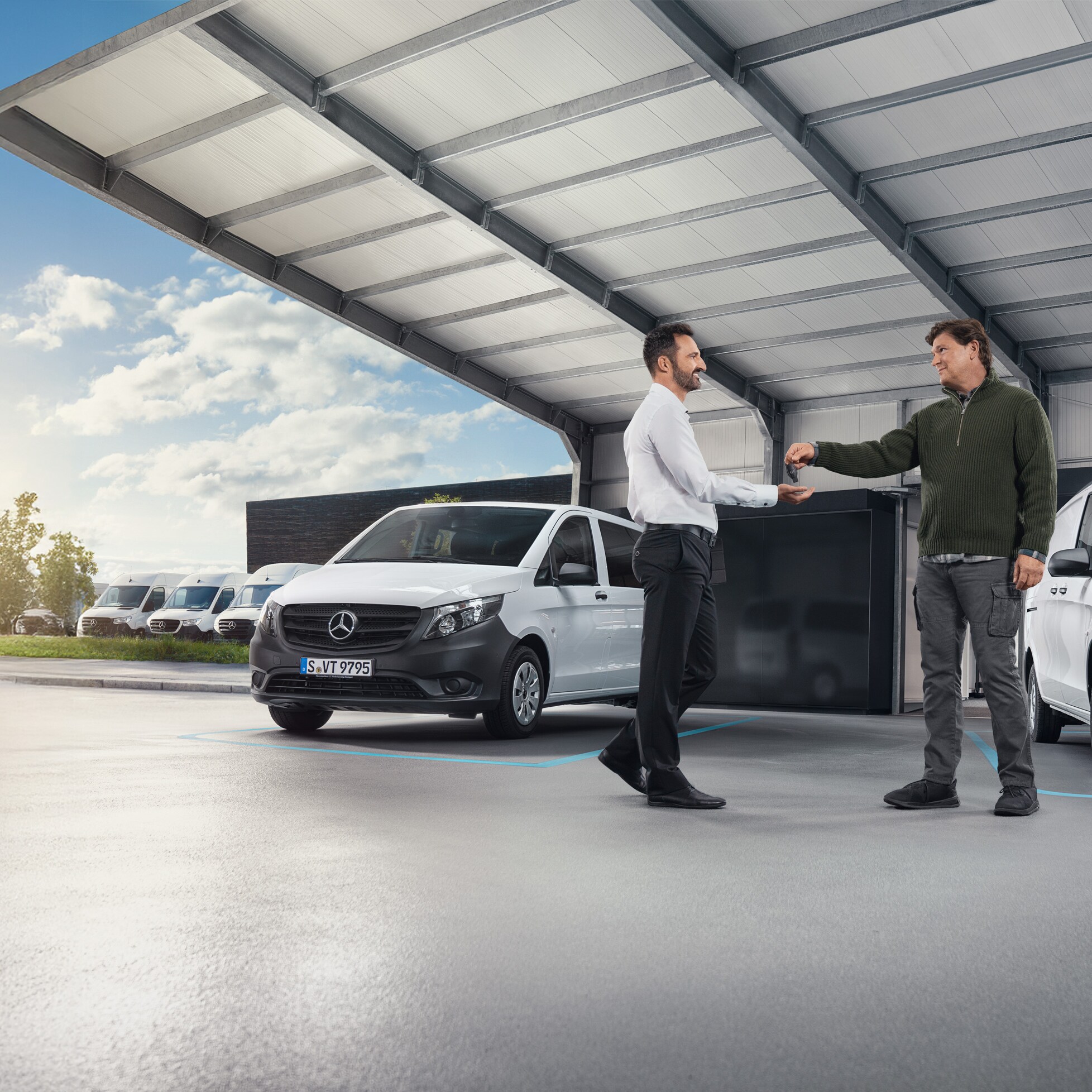 Két férfi beszélget egy csarnokban, fehér Mercedes-Benz kishaszongépjárművek előtt