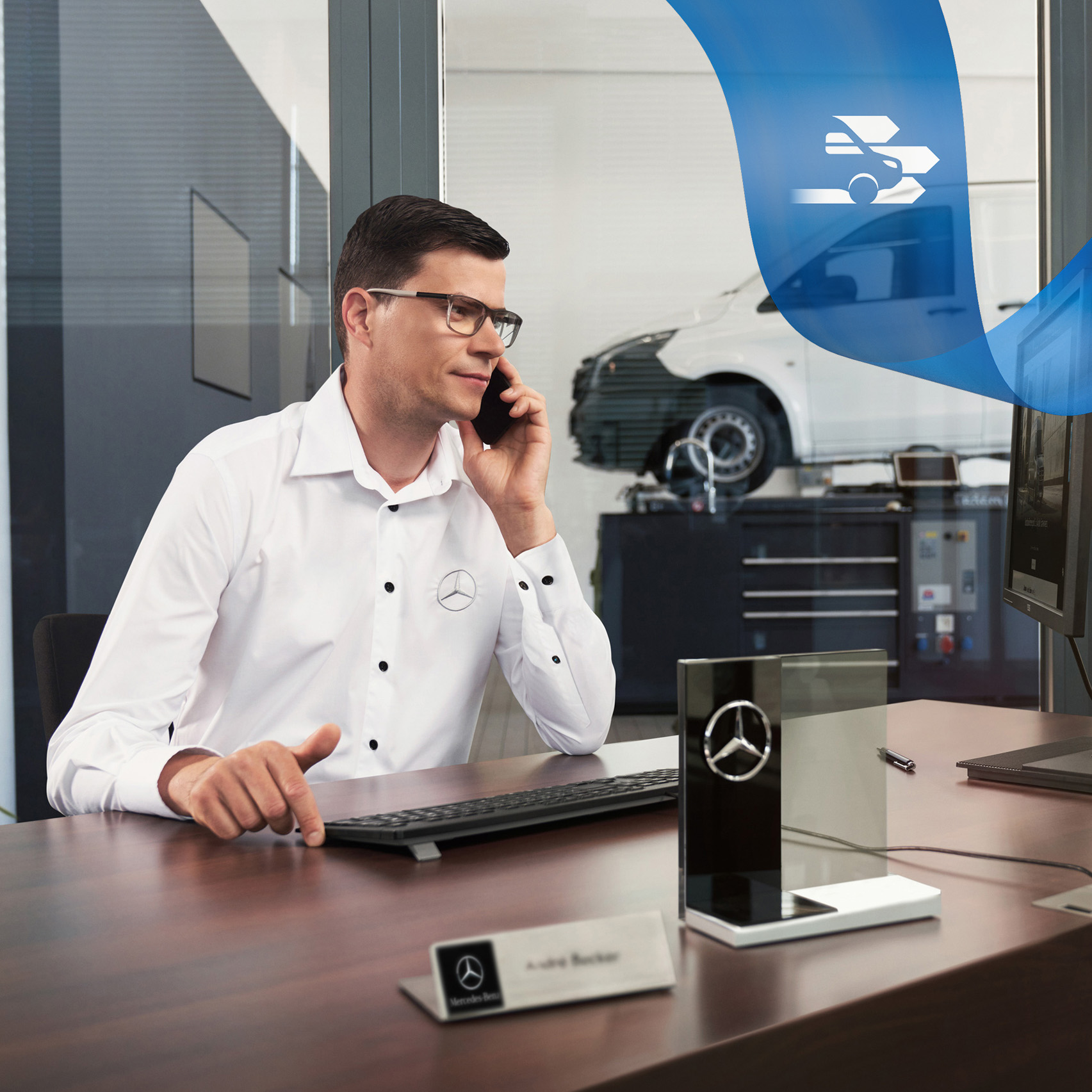 Mercedes-Benz | Vans Care | Műszaki segítségnyújtás Egy alkalmazott egy íróasztalnál telefonál, a háttérben egy Mercedes-Benz Vito a műhelyben.