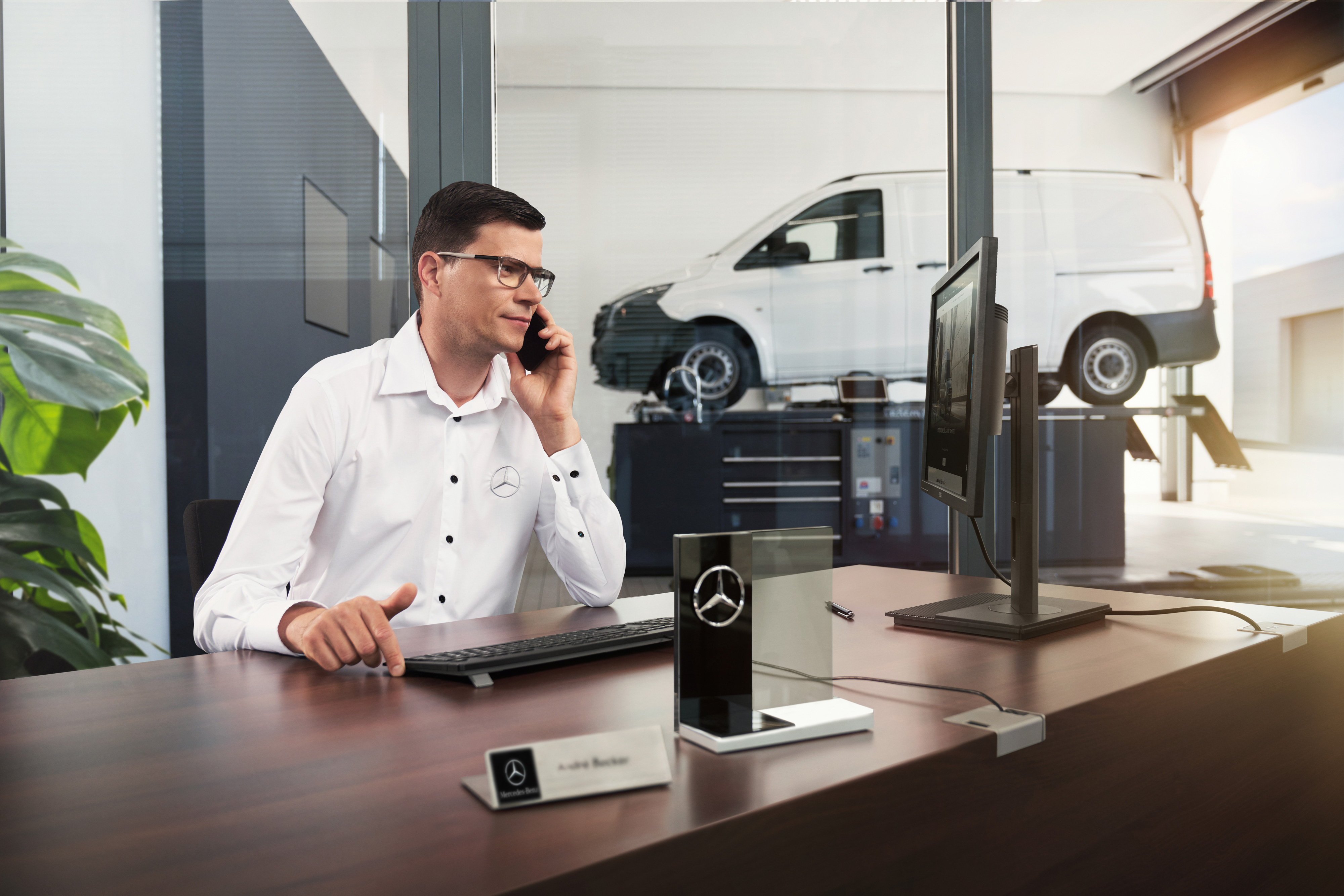 Mercedes-Benz | Komfort | Szervizpartner A Mercedes-Benz szerviztanácsadója telefonál egy műhelyben.