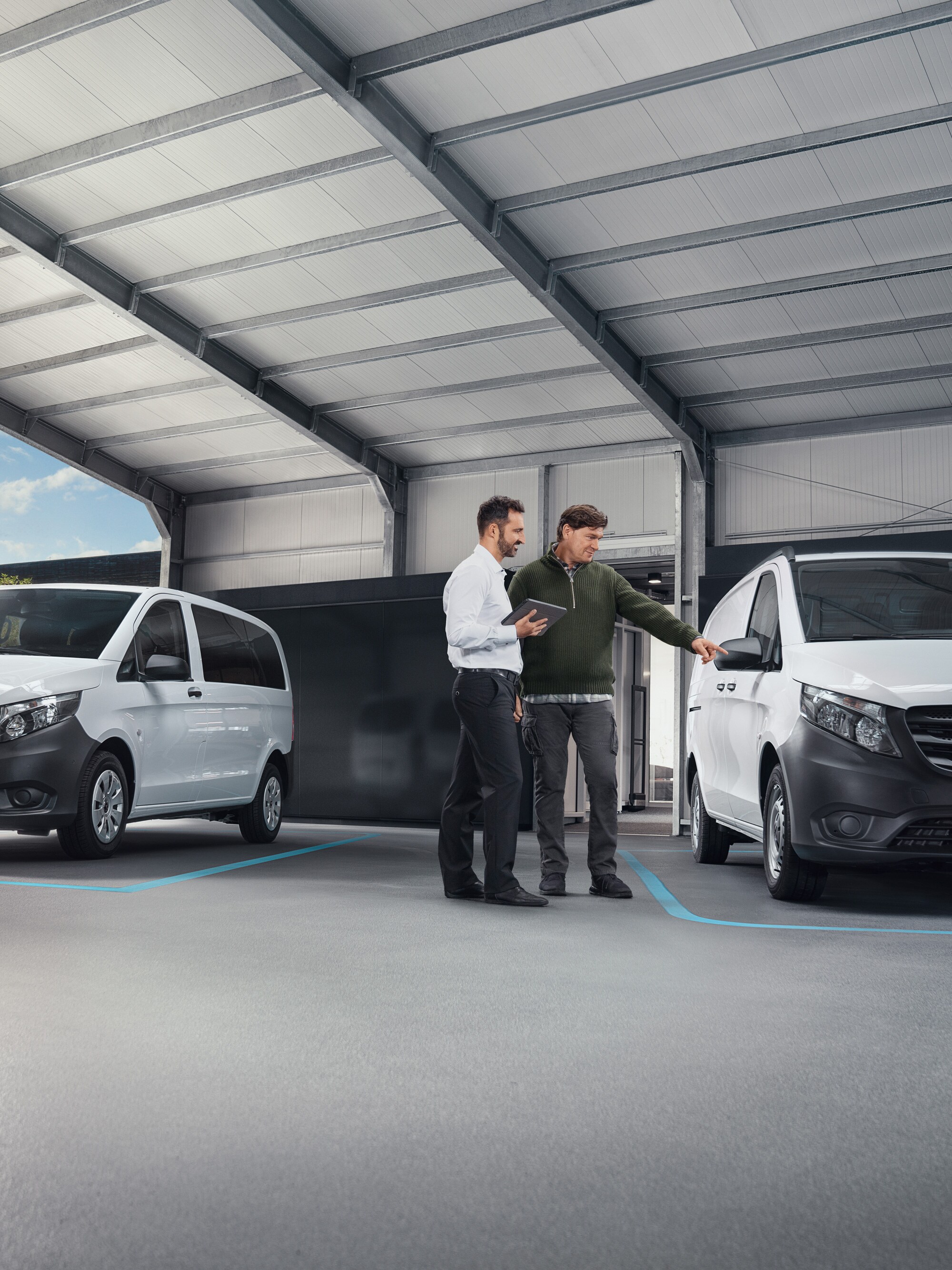 Két ember beszélget egy szervizben, két fehér Mercedes-Benz Vito előtt állva.