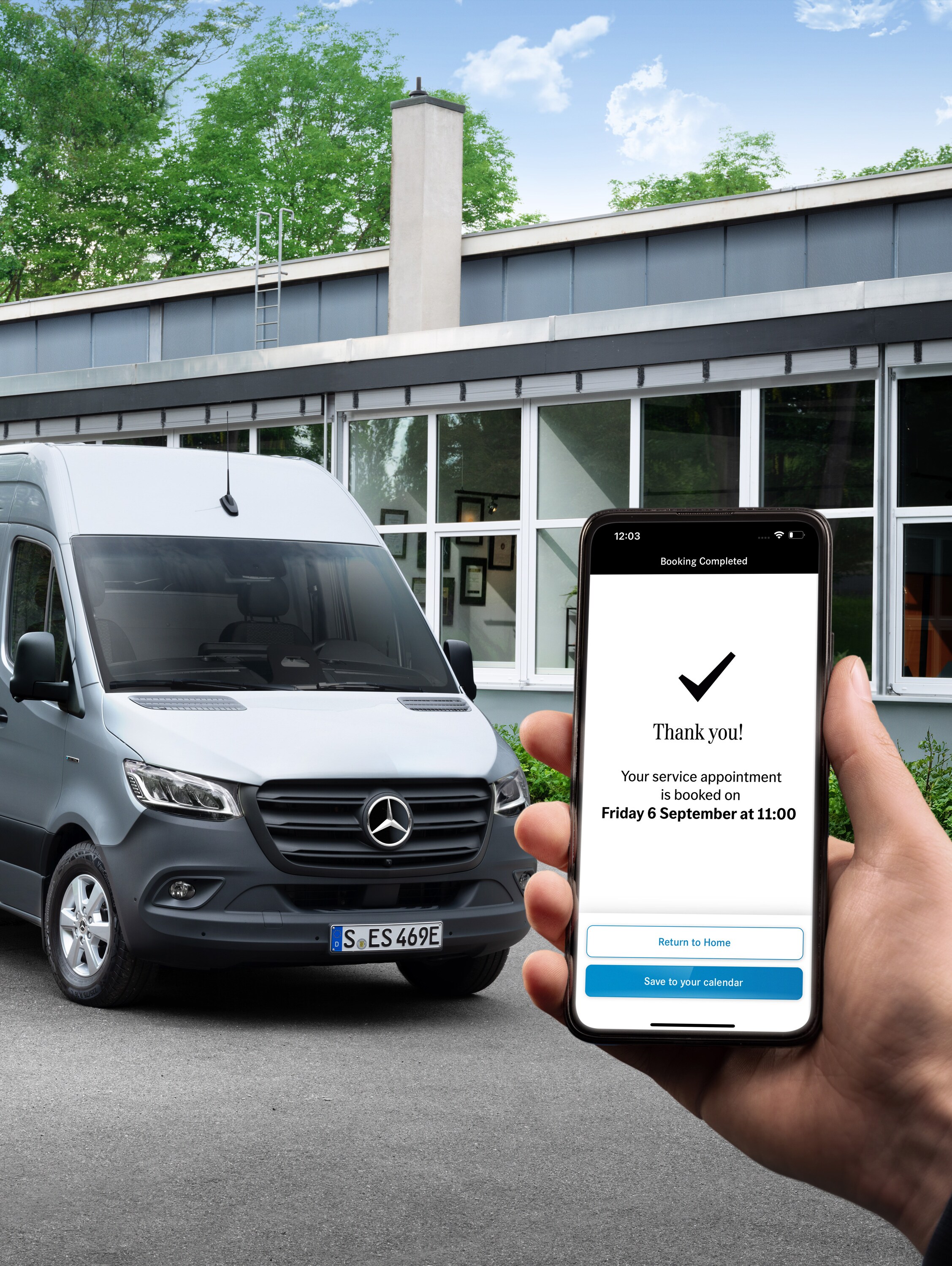 Egy szürke Mercedes-Benz Sprinter egy iroda előtt, előtérben egy okostelefont tartó emberrel.