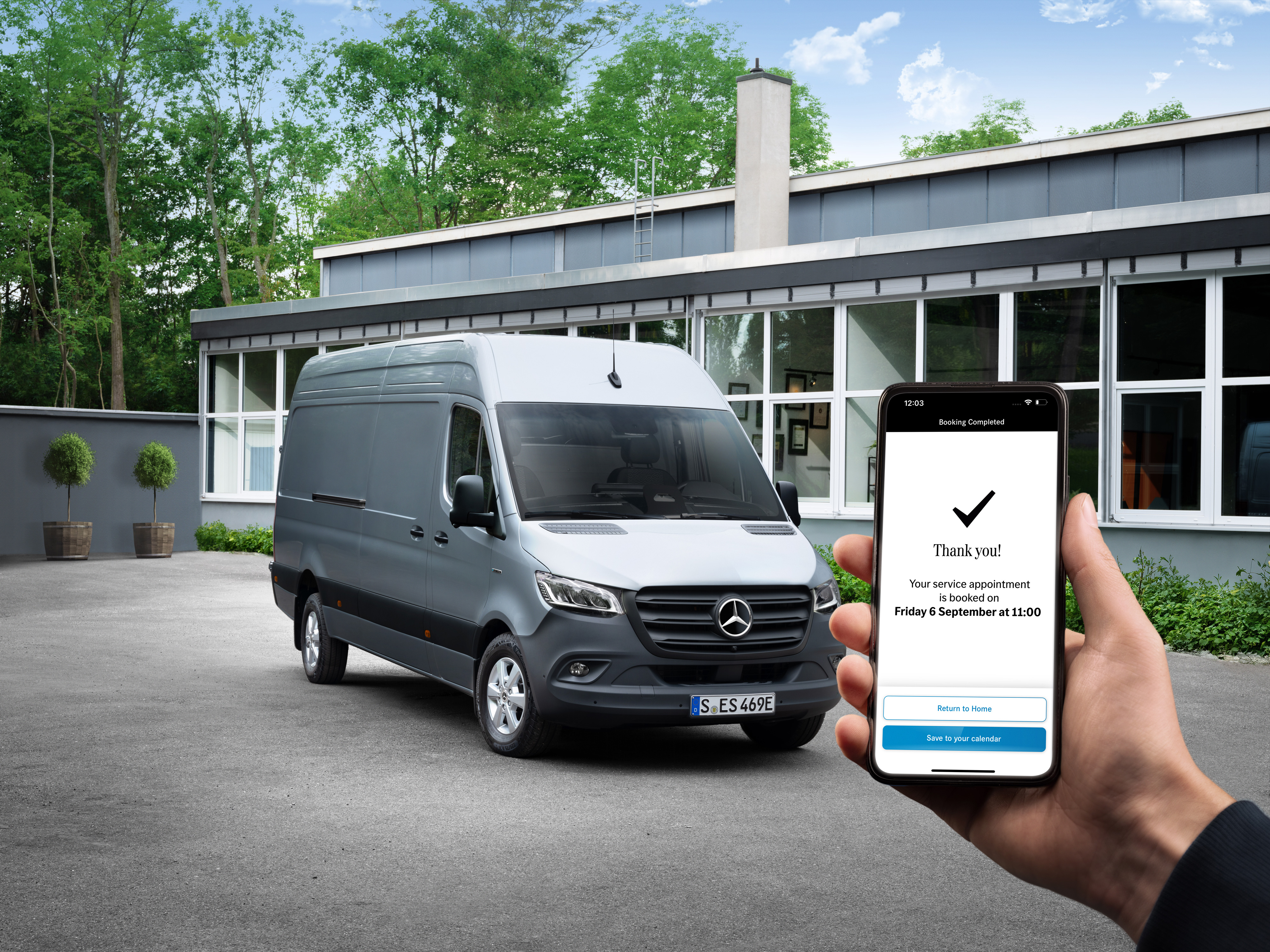 Mercedes-Benz | Komfort | Szervizpartner Egy szürke Mercedes-Benz Sprinter egy iroda előtt, előtérben egy okostelefont tartó emberrel.