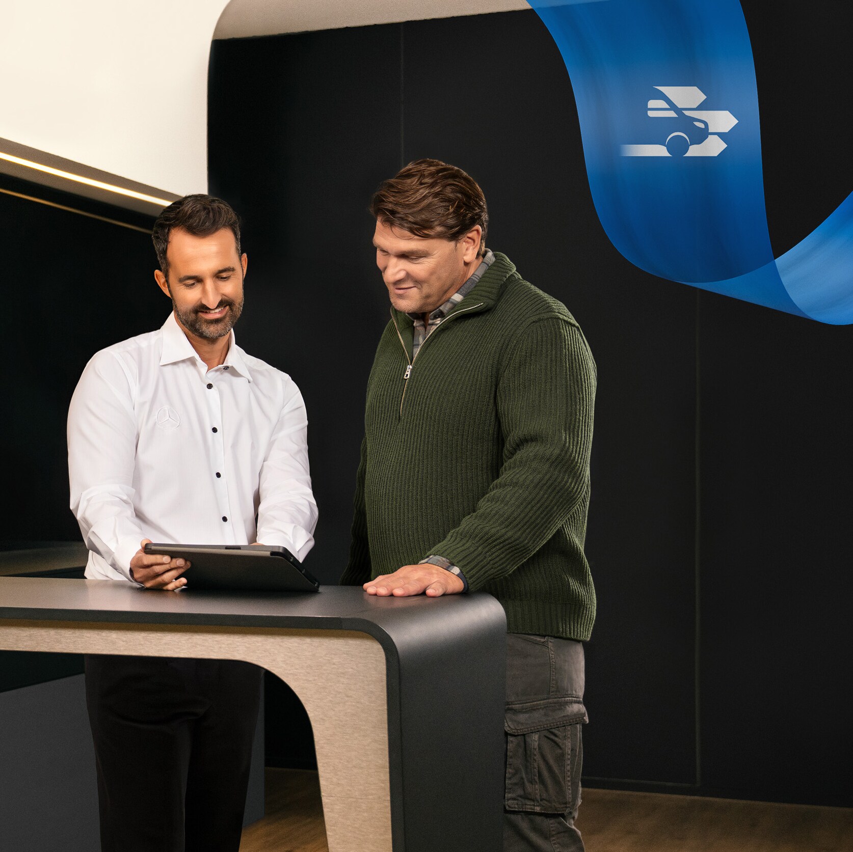 Két férfi áll egy Mercedes-Benz szervizpartner irodájában, és egy tableten látott dolgot vitatnak meg