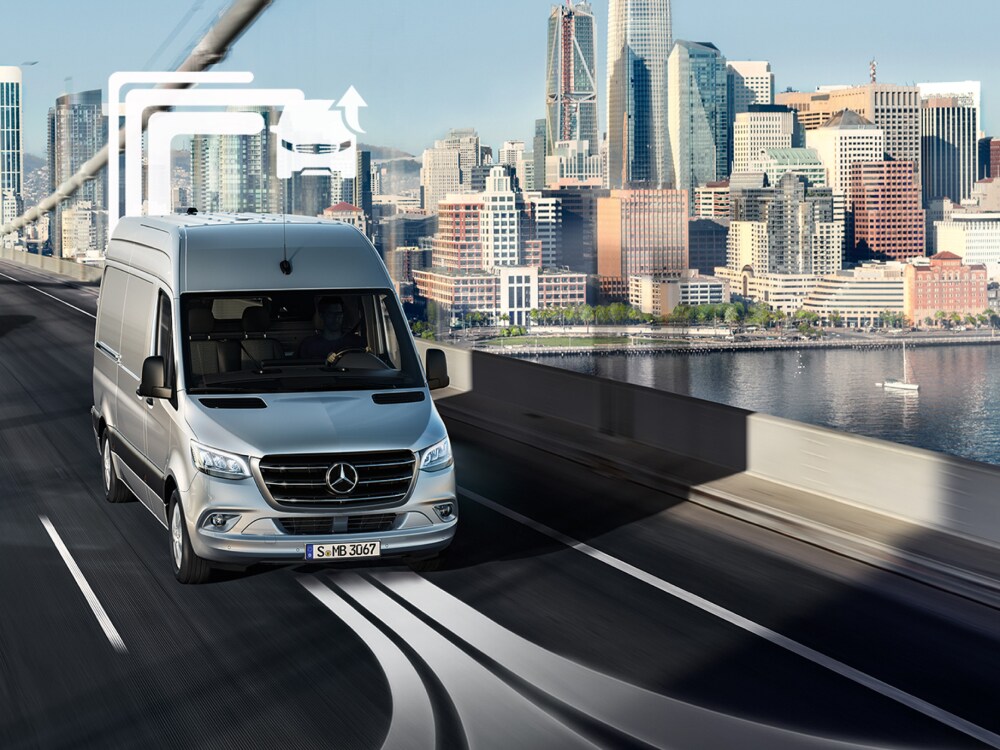 Egy Mercedes-Benz furgonszállító egy többsávos hídon halad át nappal.
