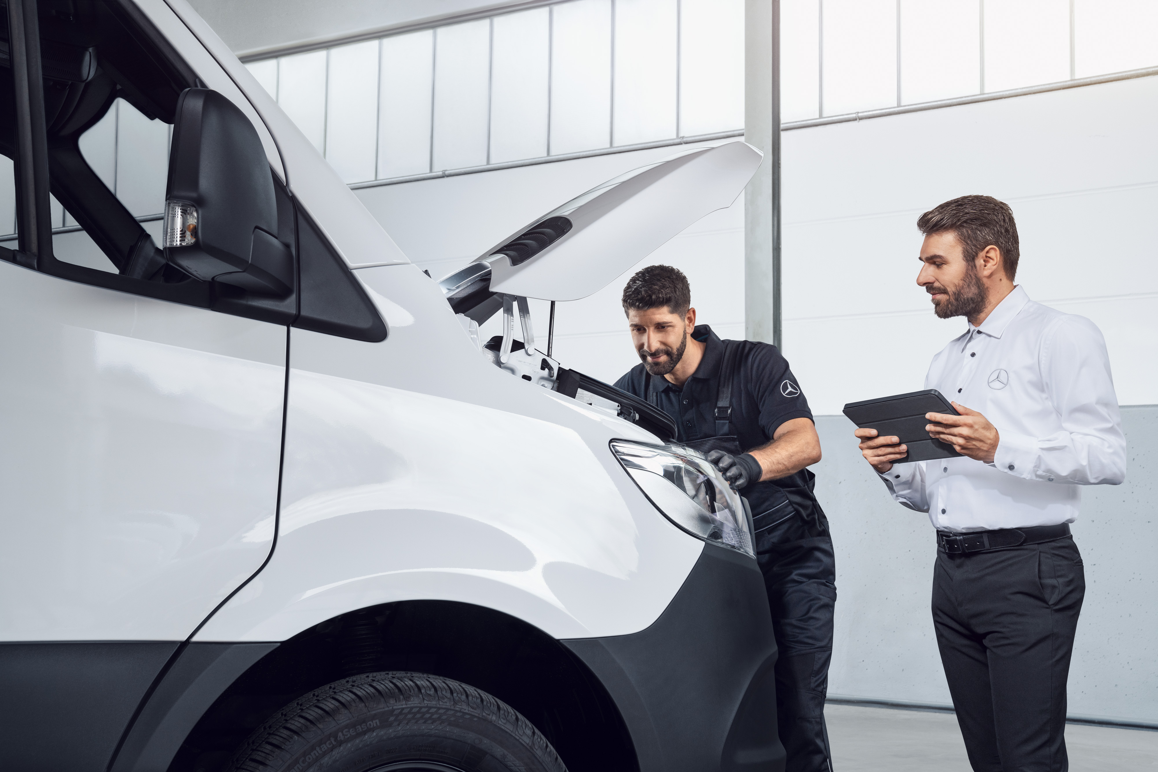 Mercedes-Benz | Kishaszongépjármű Eredeti Alkatrészek Két férfi tesztel egy Mercedes Sprintert, tablettel és nyitott motorháztetővel, téma: Mercedes-Benz Sprinter alkatrészek.