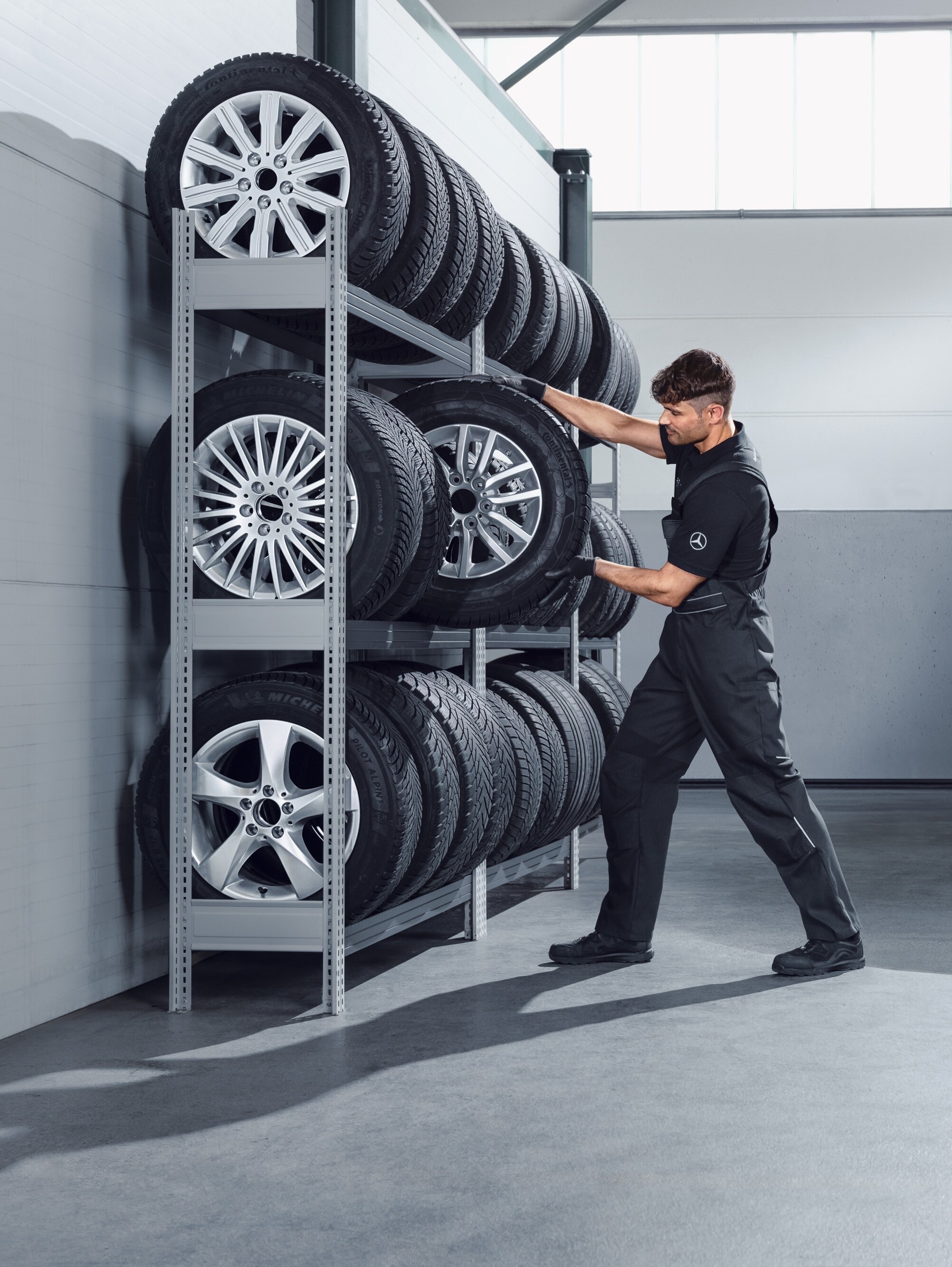 Egy szerelő kiválasztja a műhely polcáról a Mercedes-Benz komplett téli kerekeket egy fehér Sprinterhez.