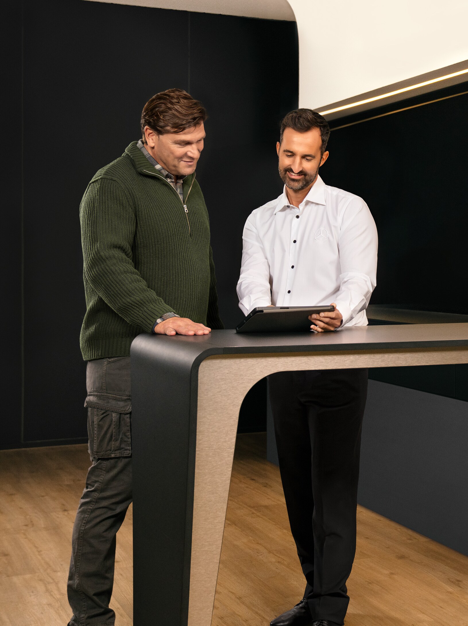 Két férfi konzultál egy asztal körül állva, egy iPadet nézve.