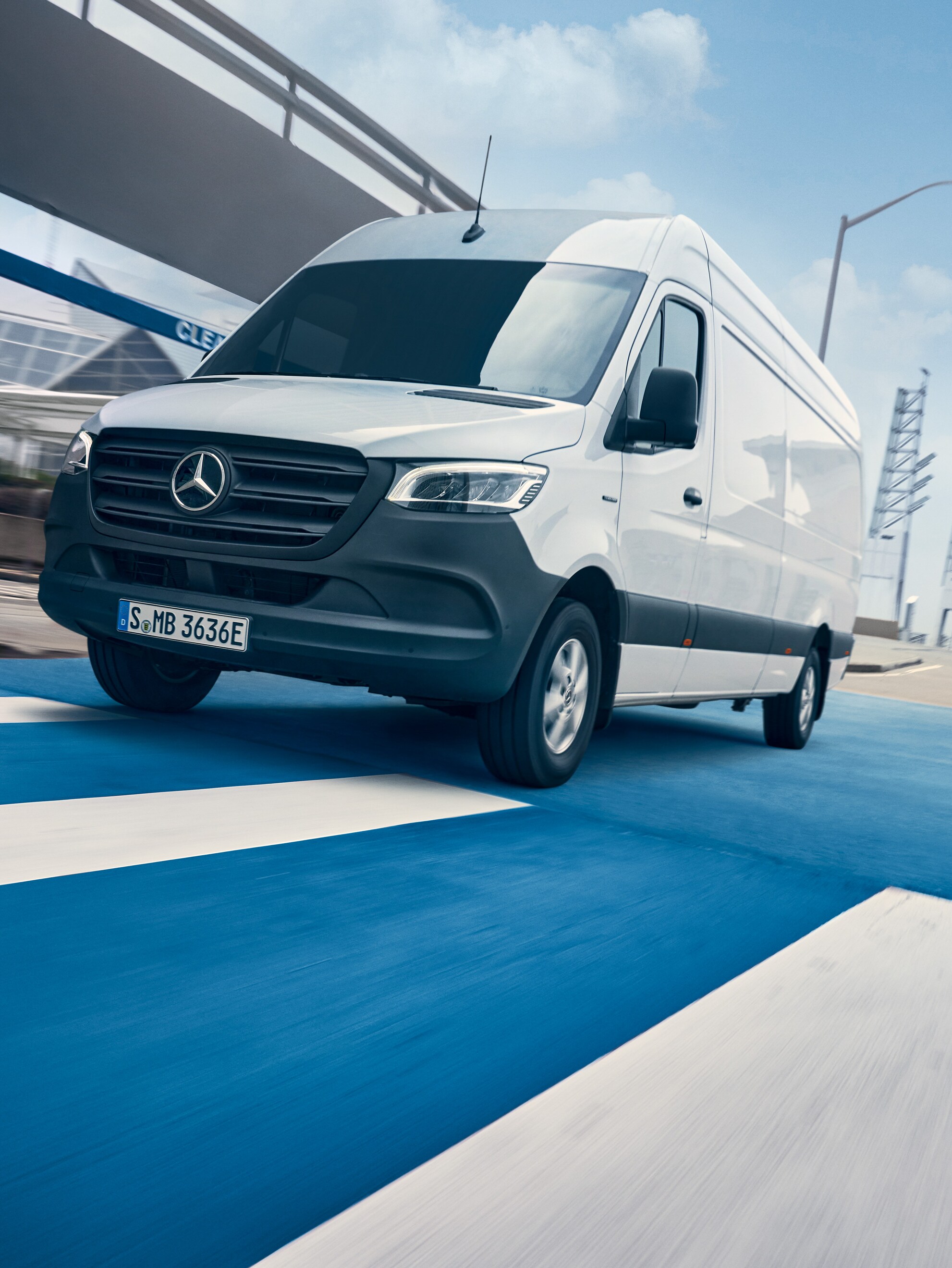 Egy fehér Mercedes-Benz Sprinter halad a városon átvezető úton.