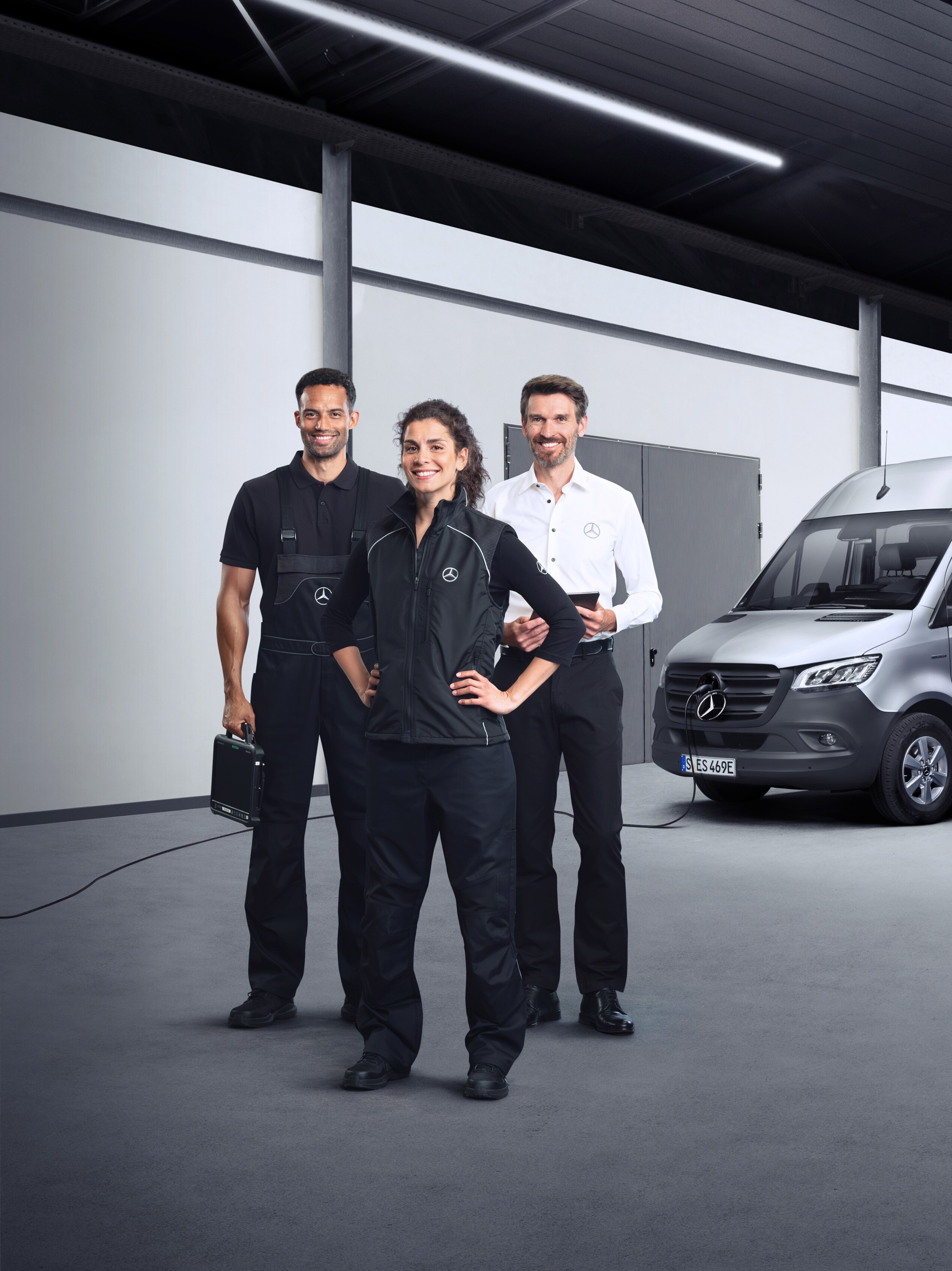 Három alkalmazott áll egy ezüstszínű Mercedes-Benz eSprinter előtt, csatlakoztatott töltőkábellel.