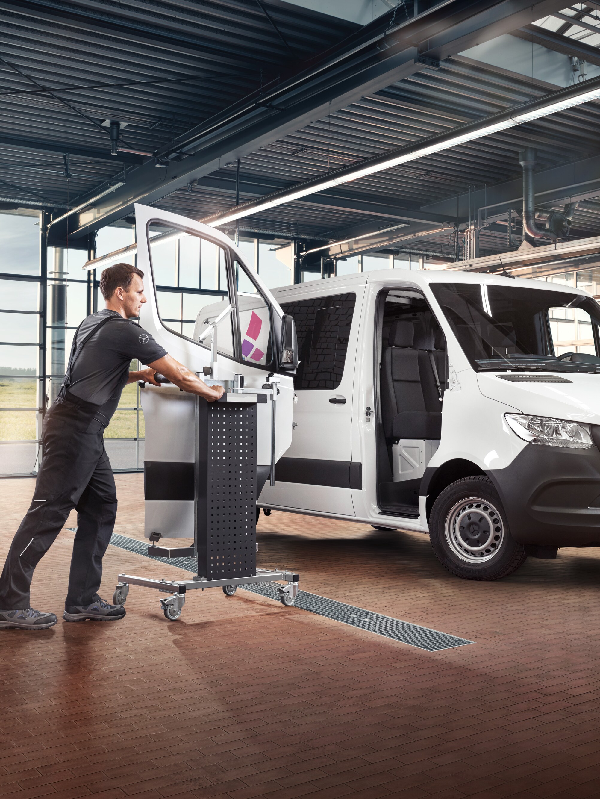 Egy technikus leveszi egy fehér Mercedes-Benz Sprinter  utasoldali ajtóját.
