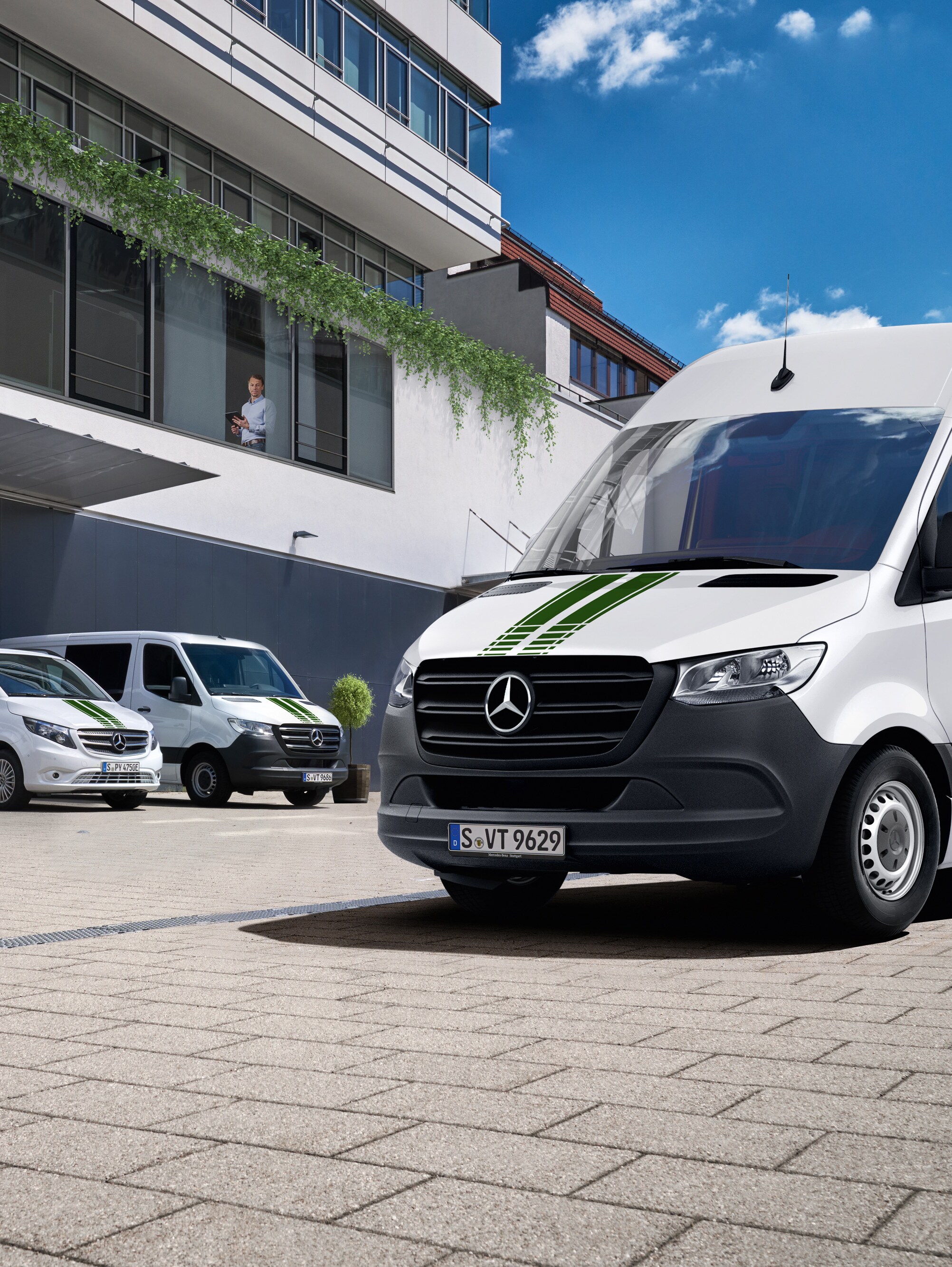 Fehér Mercedes-Benz kishaszongépjárművek flottája egy irodaház előtt egy napsütéses, kék égboltú napon.