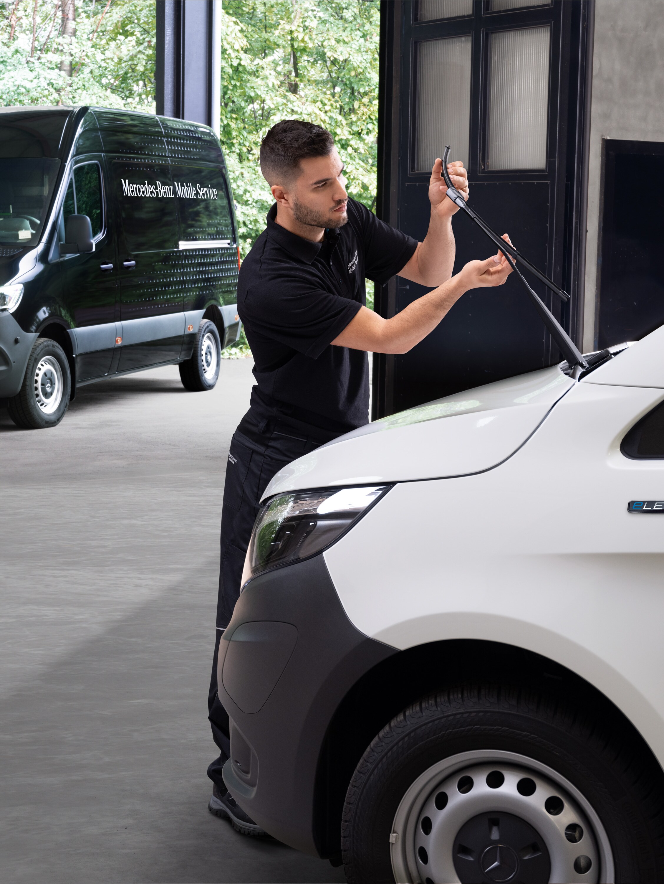 Egy szerelő ablaktörlő lapátokat cserél egy fehér Mercedes-Benz Vito-n.