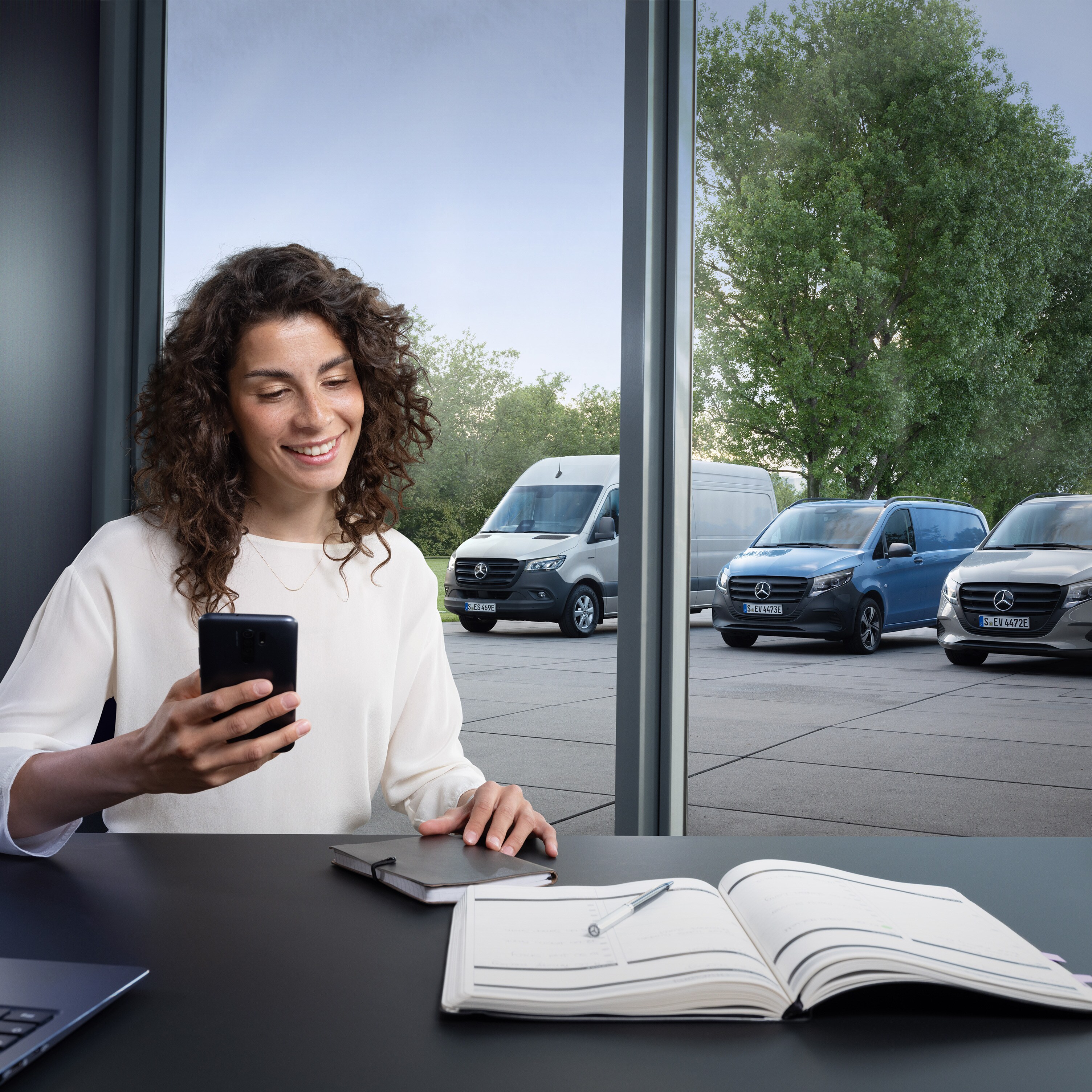 Woman planning on her smartphone in front of a range of Mercedes-Benz vans in the background.