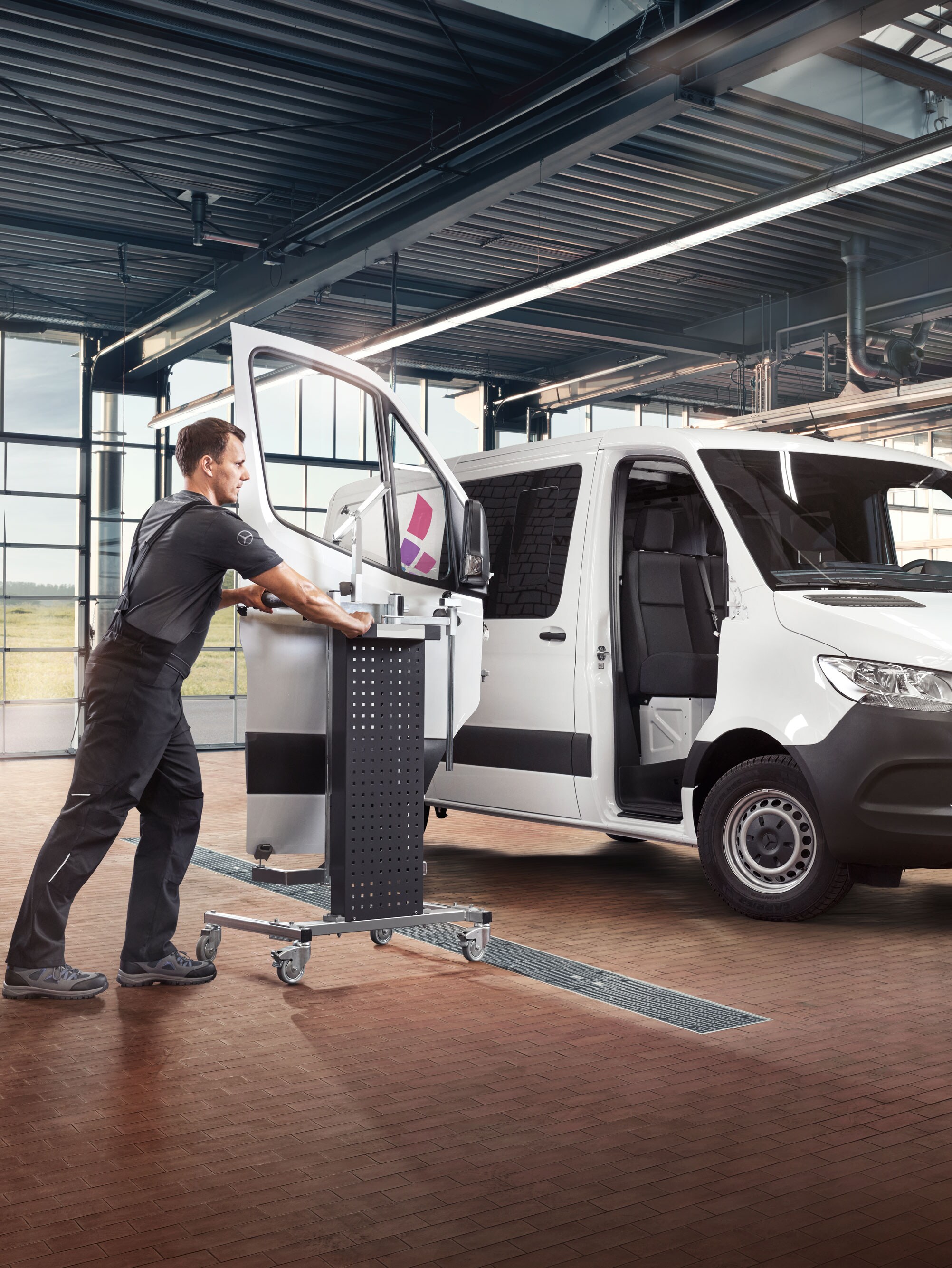 Egy szerelő szereli az ajtót egy fehér Mercedes-Benz Sprinteren.