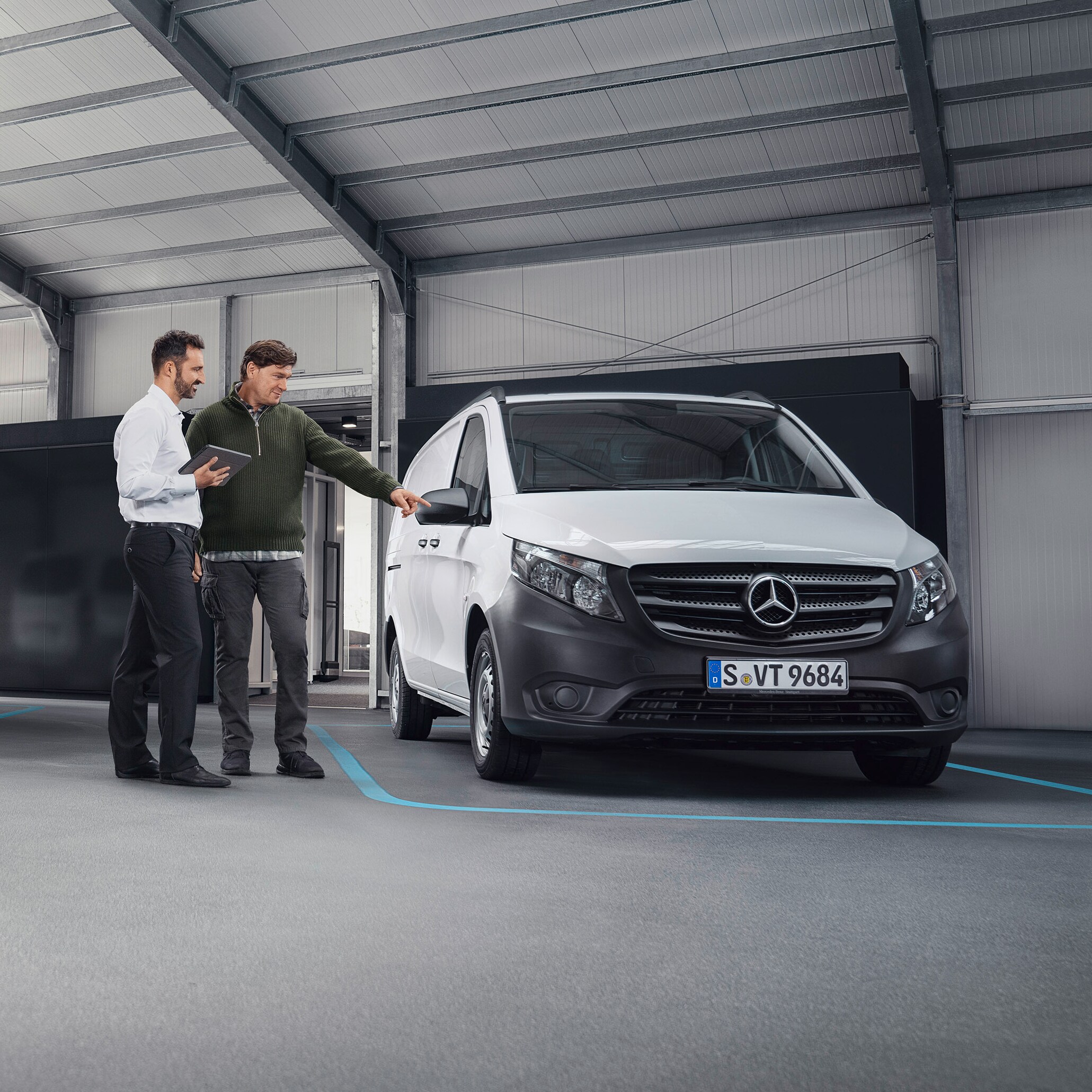 Mercedes-Benz ügyfélszolgálati ügyintéző az ügyféllel egy szervizpartnernél egy kishaszongépjármű előtt.