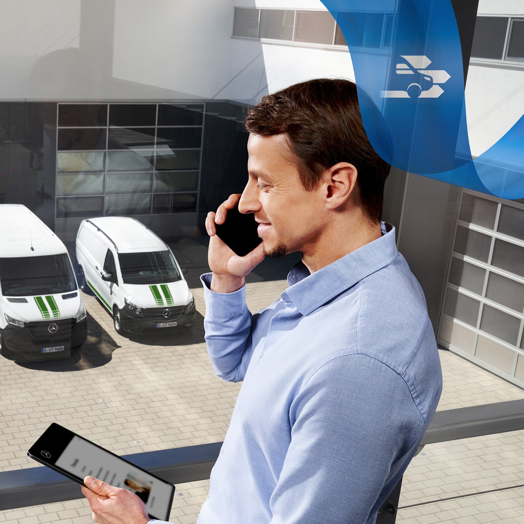 Egy férfi telefonál, miközben egy tabletet néz, a háttérben Mercedes-Benz kishaszongépjárművek sora.