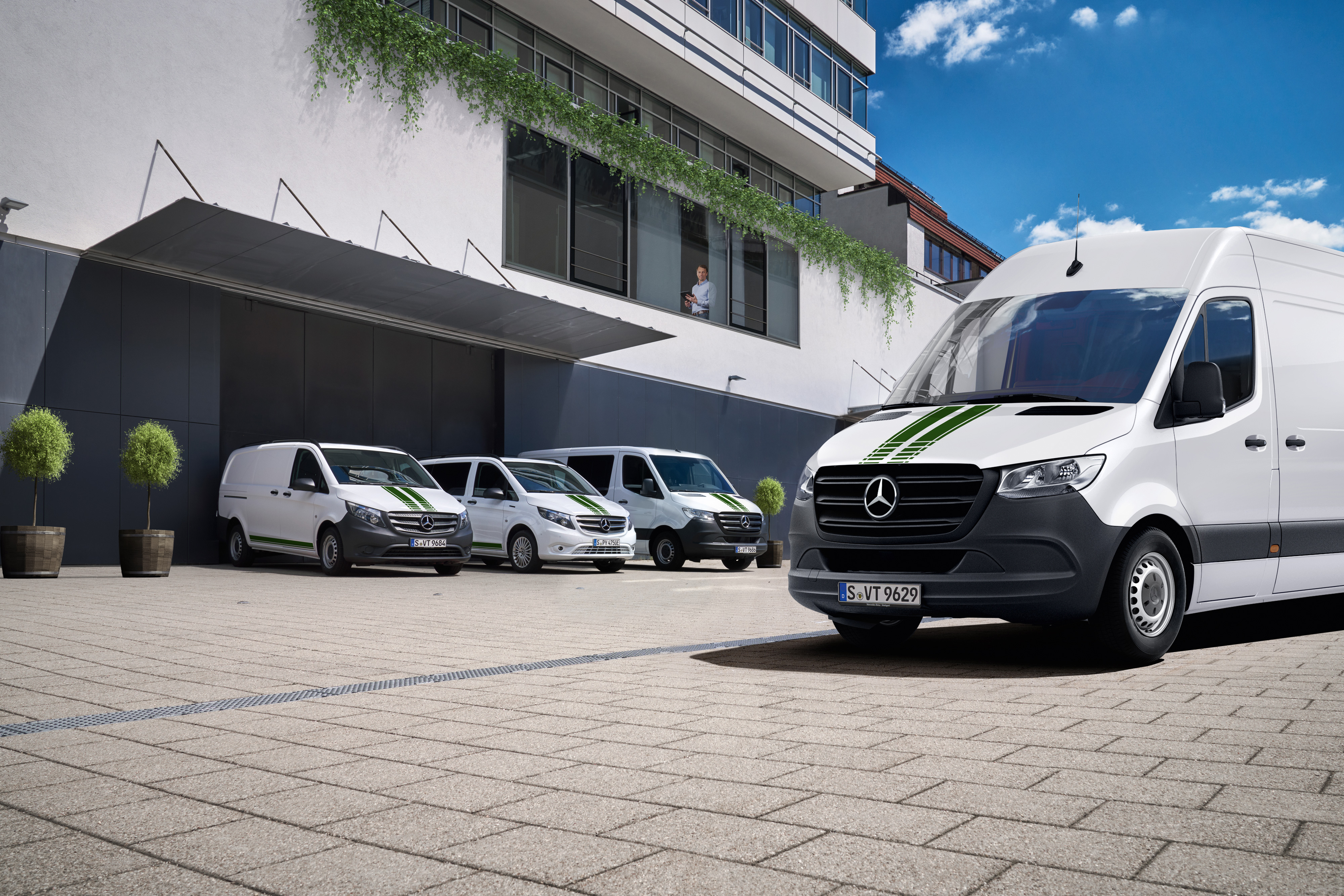Mercedes-Benz | Transzporter-technológia | Van Uptime Monitor Mercedes-Benz kishaszongépjárművek flottája egy épület előtt, a digitális flottafelügyeletet szimbolizálva.