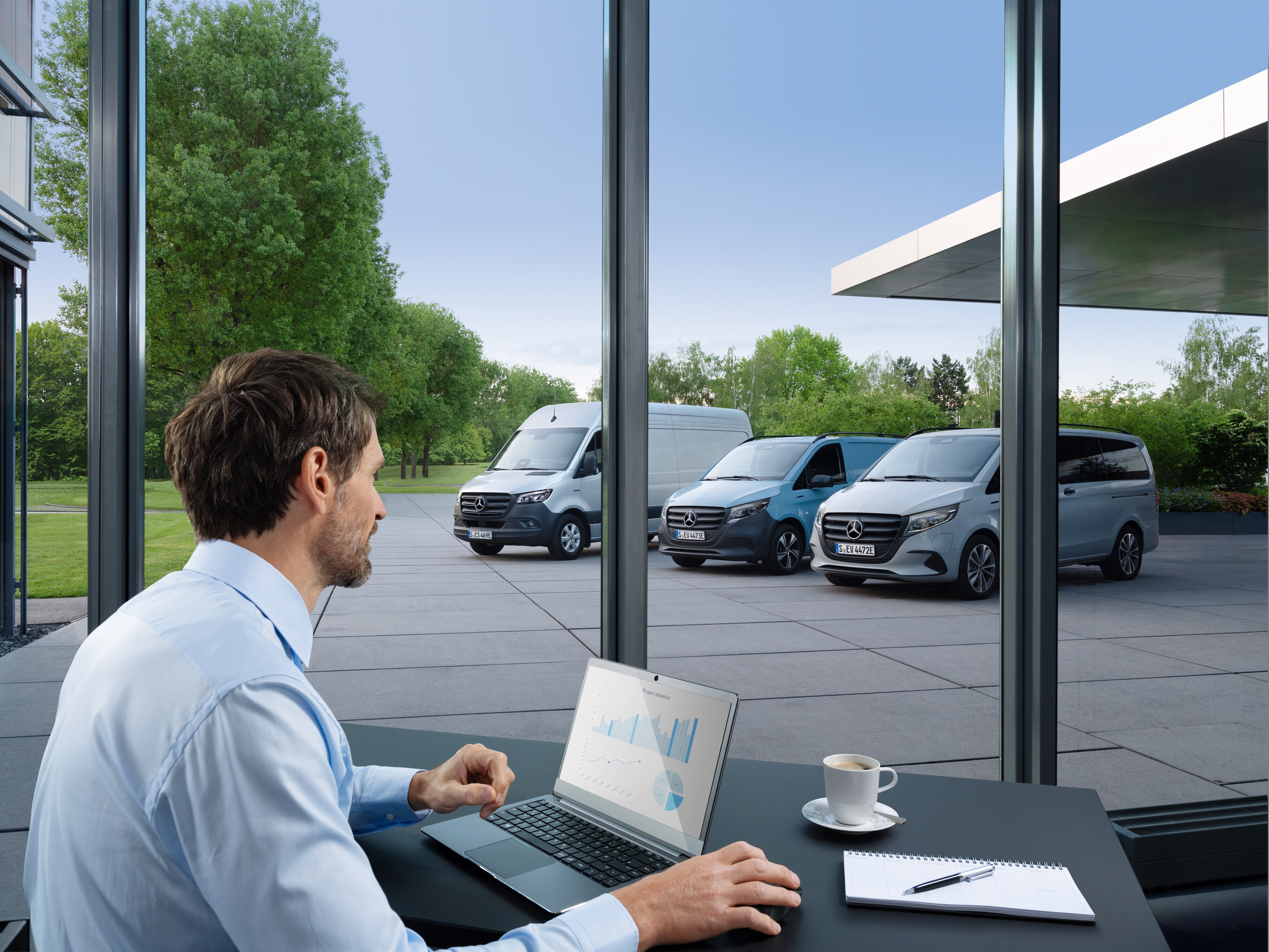 Egy férfi laptop segítségével több parkoló Mercedes-Benz transzportert figyel, a digitális flottakezelés szimbóluma.