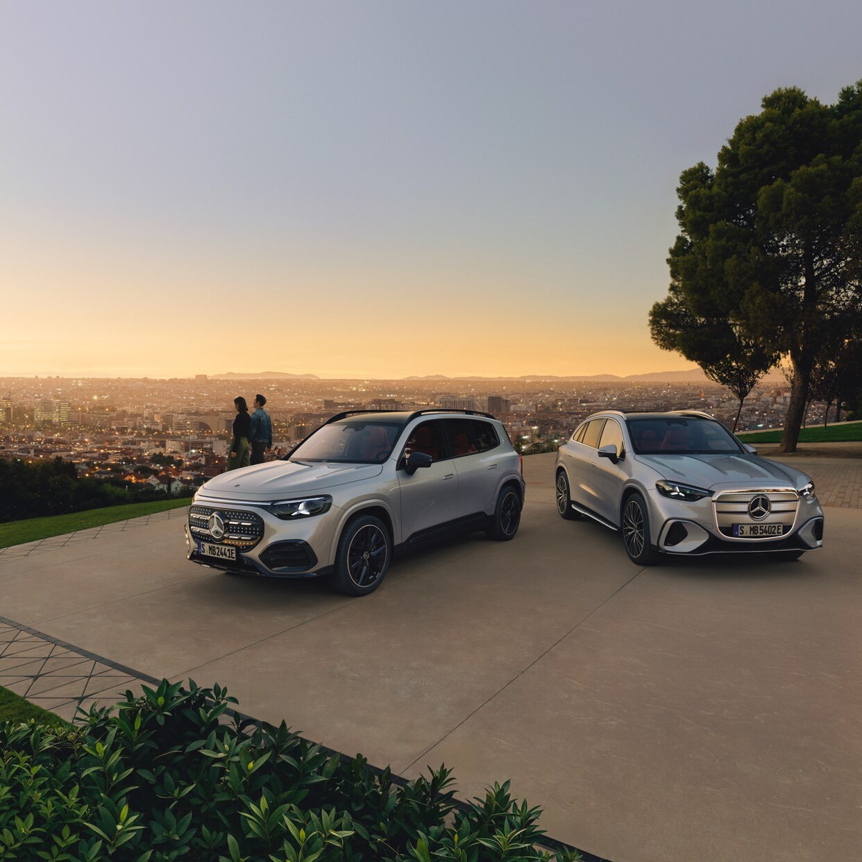 Mercedes-Benz elektromos GLB és GLCés egy pár egy erdős magaslaton a város fölött.