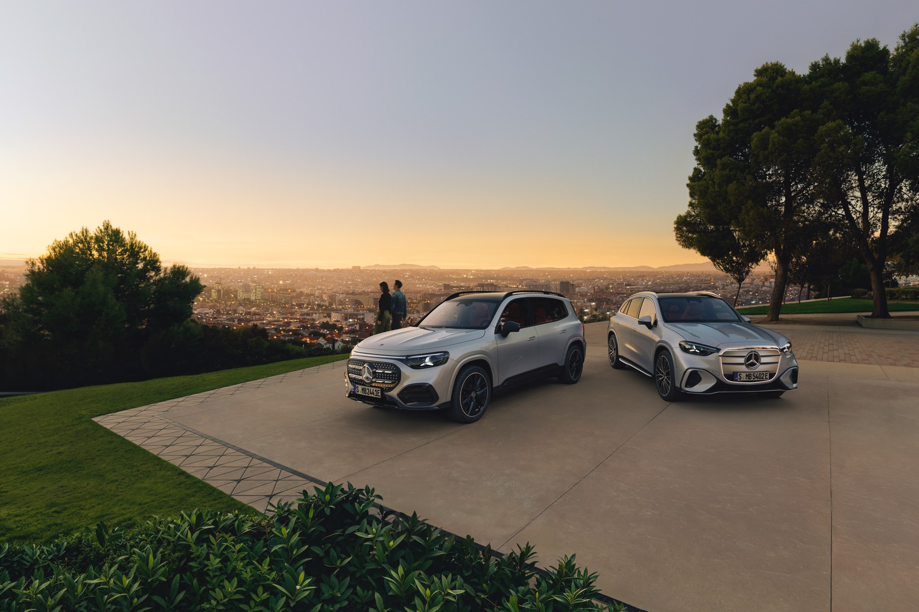 Mercedes-Benz elektromos GLB és GLCés egy pár egy erdős magaslaton a város fölött.