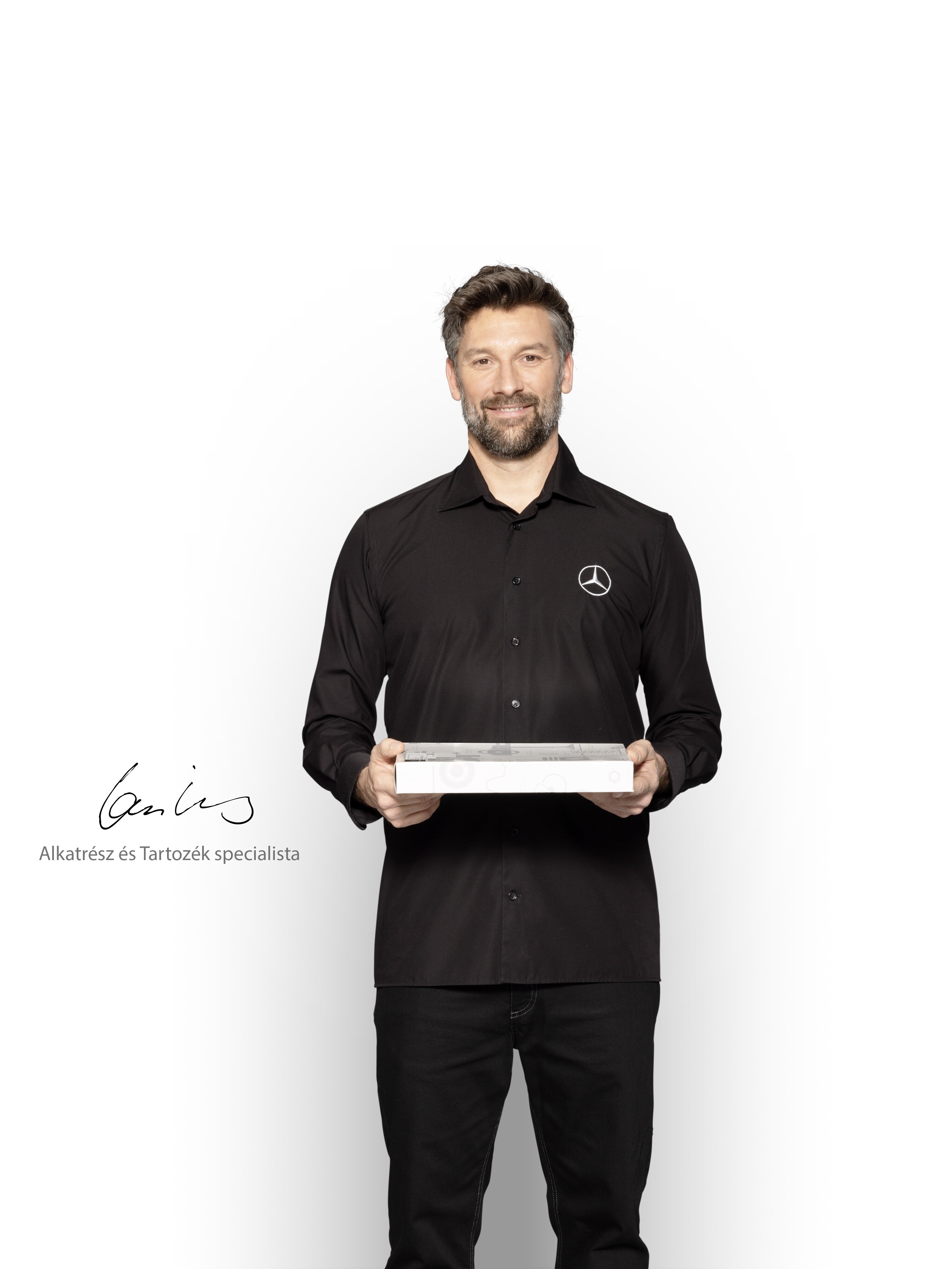 A Mercedes-Benz szerelő egy dobozzal a kezében mutatja a Mercedes-Benz eredeti alkatrészeit.